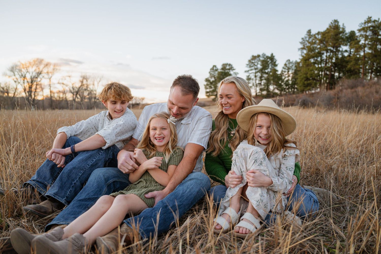 Family sitting together in tall grass field during golden hour sunset photo session.