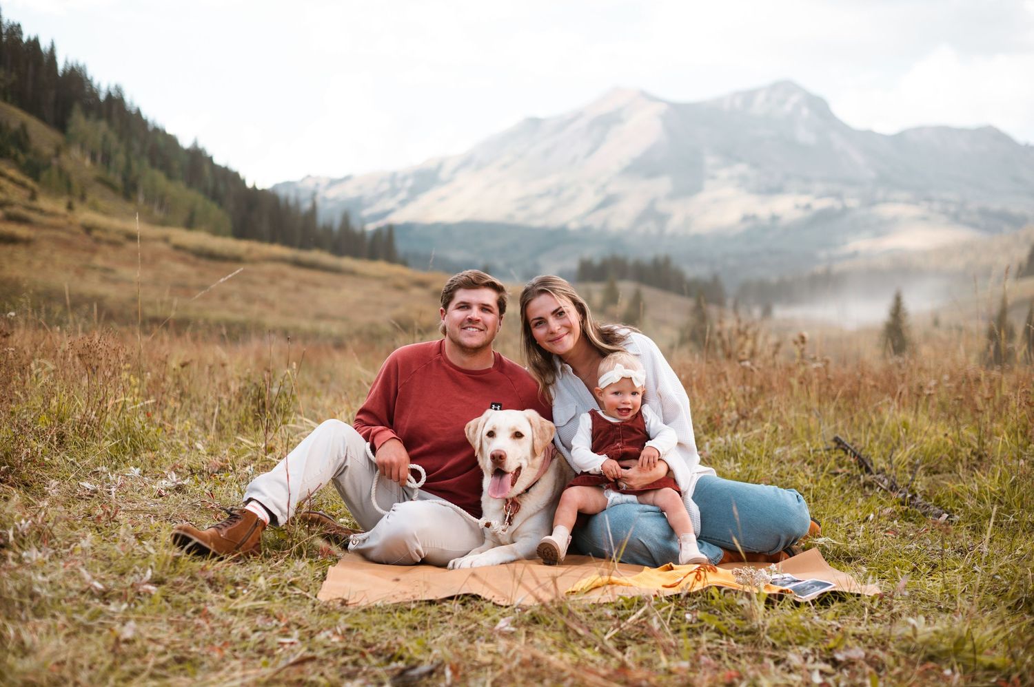 Family with baby and dog in the Crested Butte Mountains, enjoying a scenic hike pregnancy announcement photos with white lab