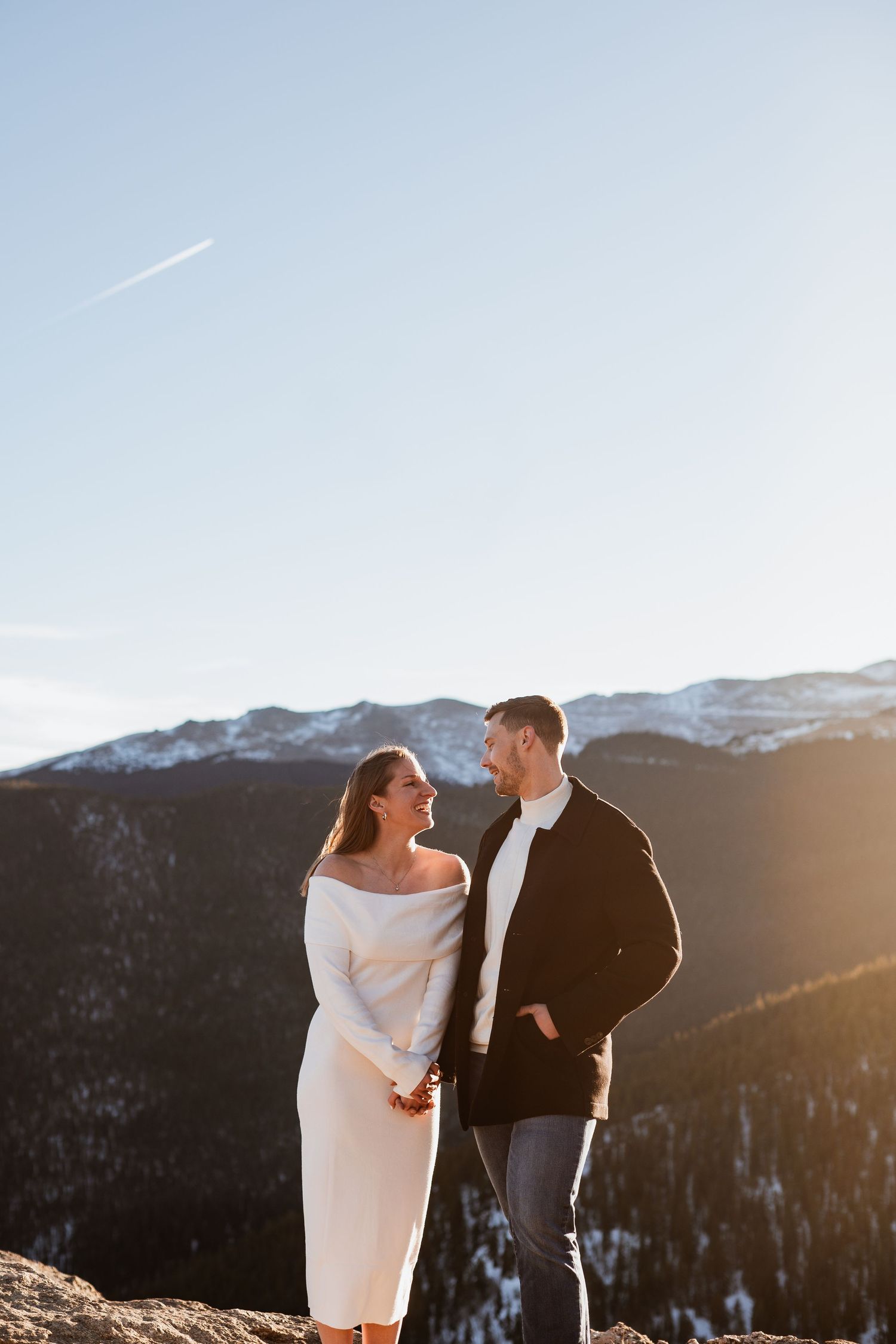 An engaged couple stands on a cliff in Evergreen, Colorado, with majestic mountains as the perfect backdrop, capturing their love and advent