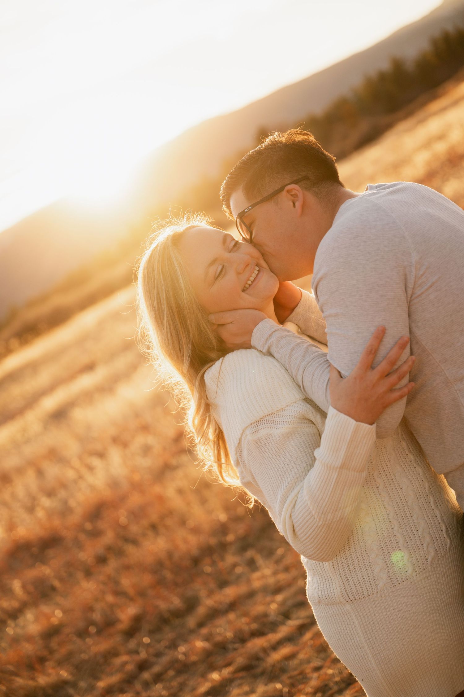 A couple embraces in a golden sunlit field during sunset creating a romantic silhouette against the warm glowing sky.