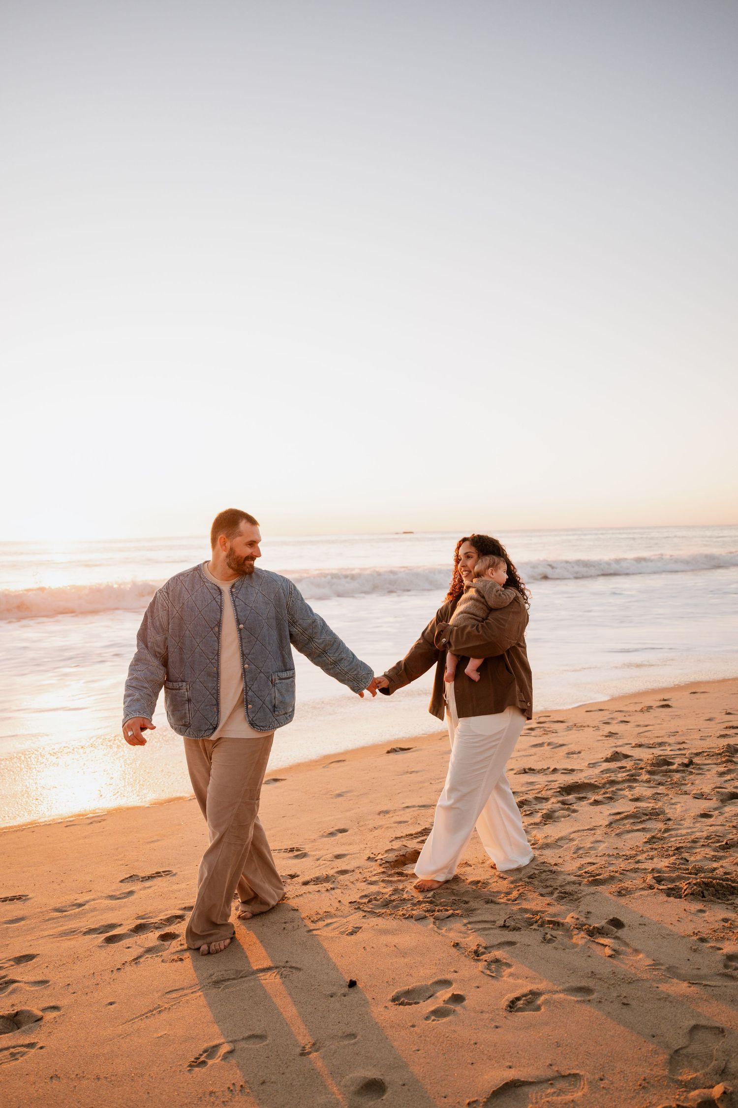 A couple dances playfully together on a sandy beach at sunset with warm golden light illuminating the scene.