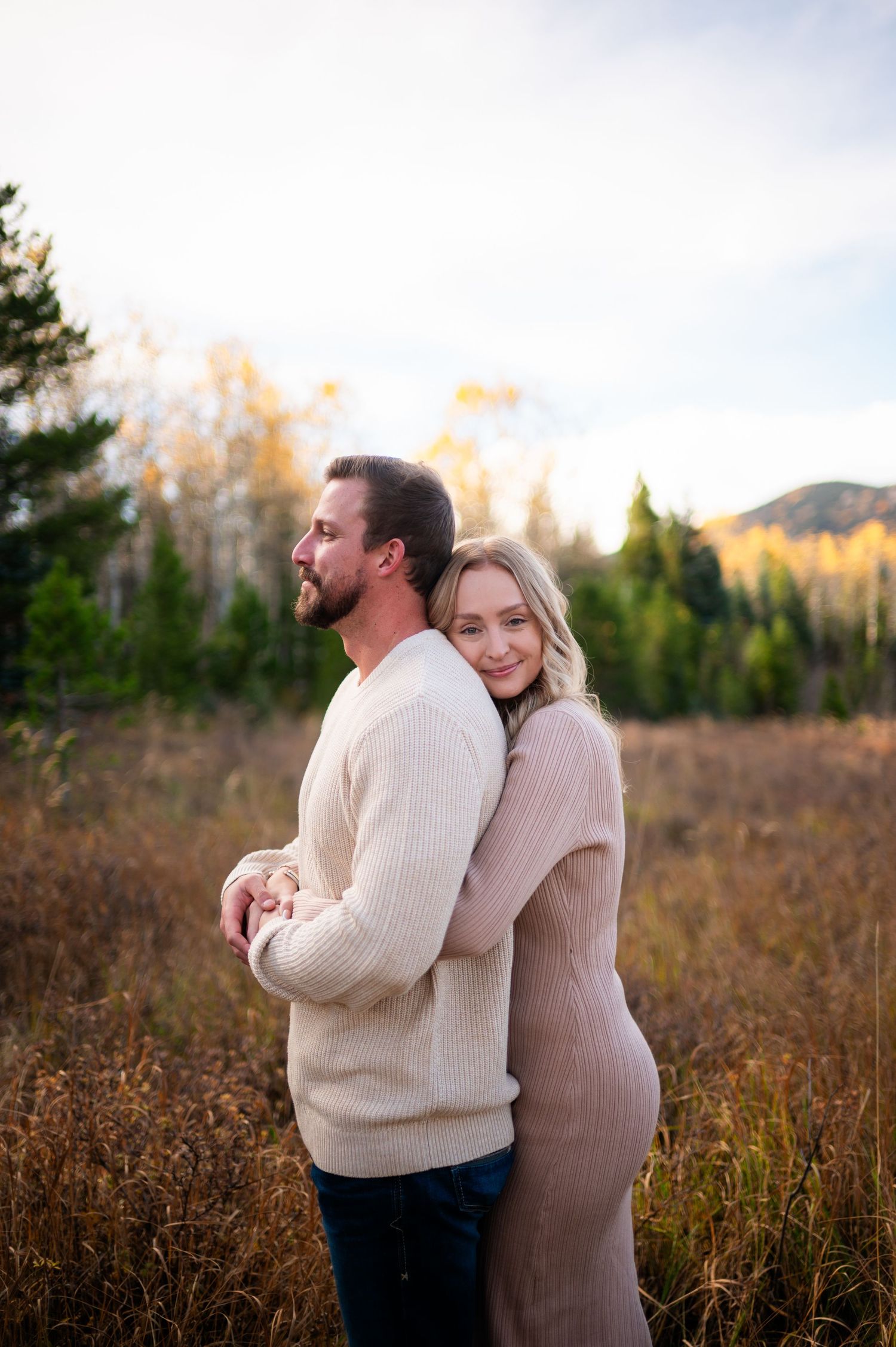 A couple in cozy sweaters share intimate moments in a golden autumn field during sunset.