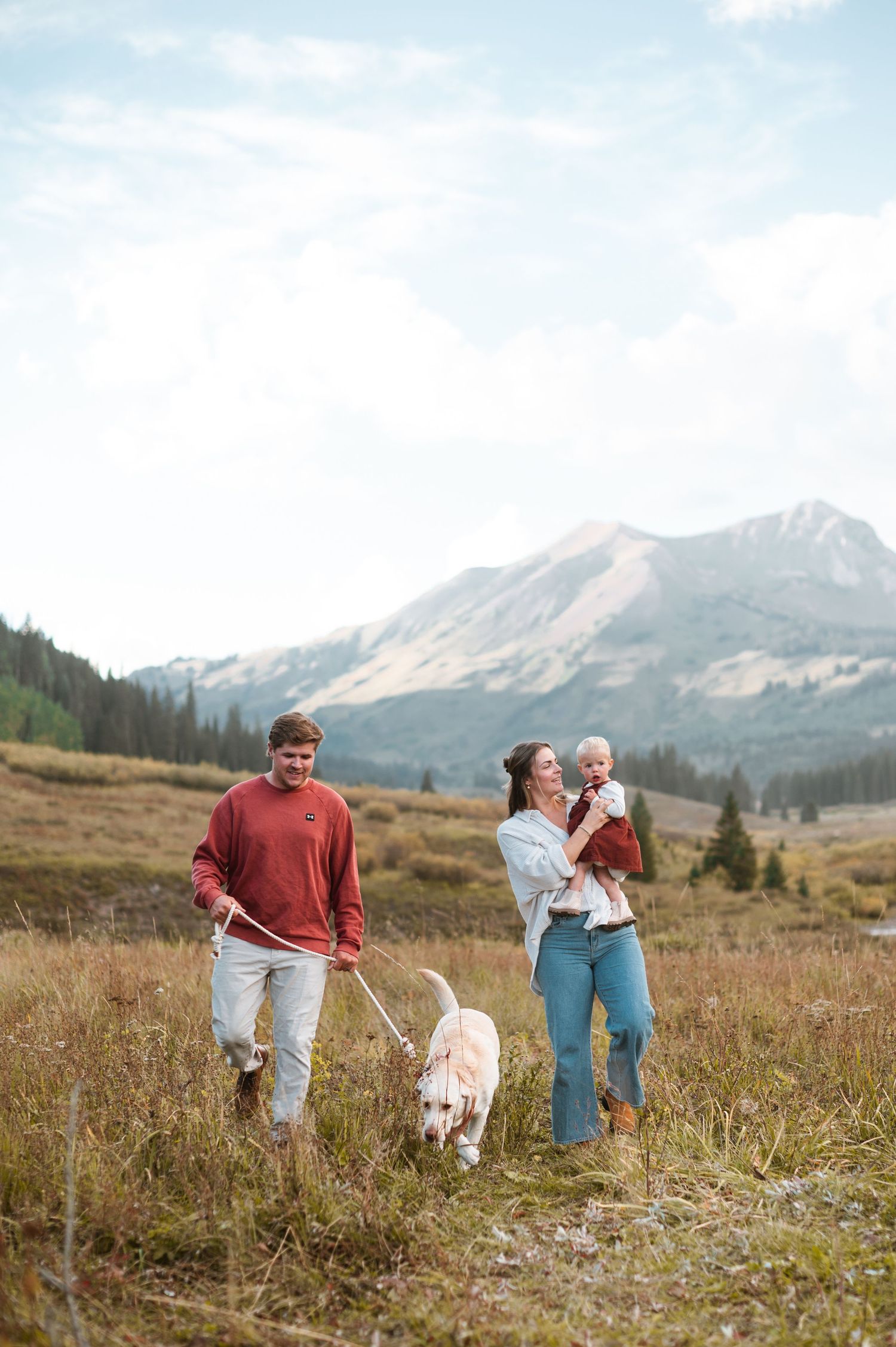 Family with baby and dog in the Crested Butte Mountains, enjoying a scenic hike pregnancy announcement photos with white lab