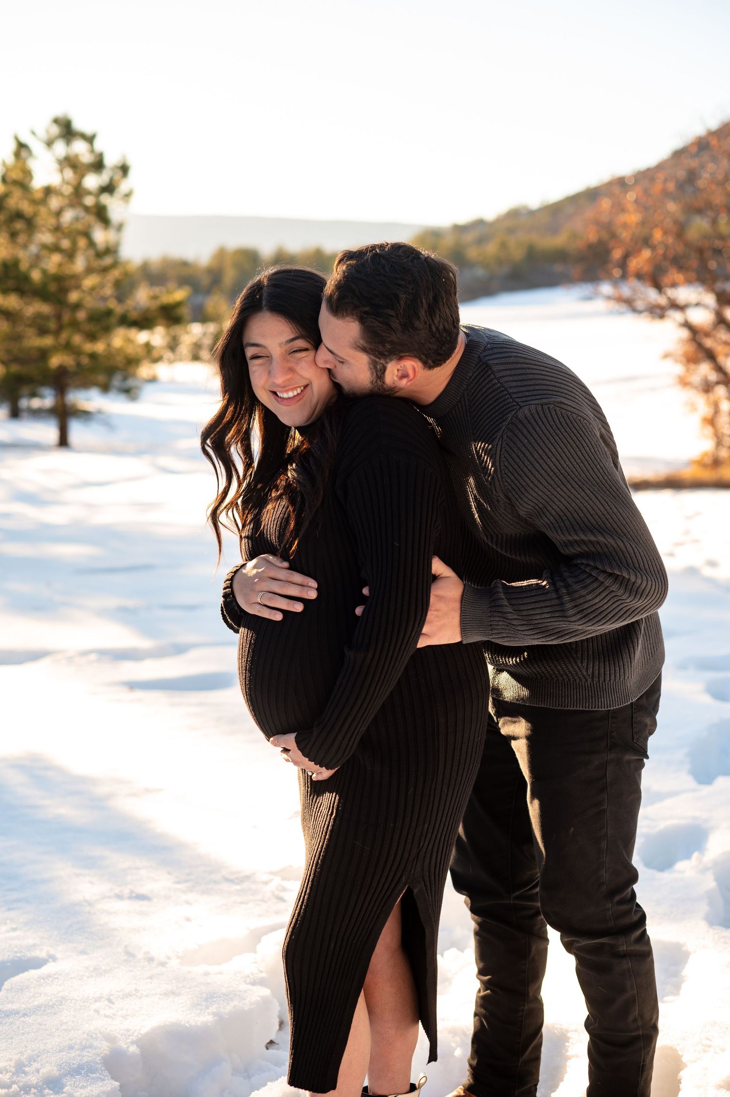 A glowing couple embraces the winter chill, their love and excitement shining through the snow as they await their little one’s arrival