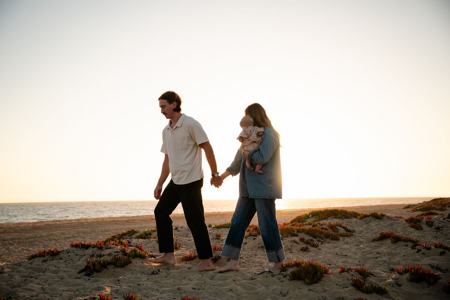 Couple walking along scenic coastal cliffs at sunset while holding hands and enjoying the ocean view.