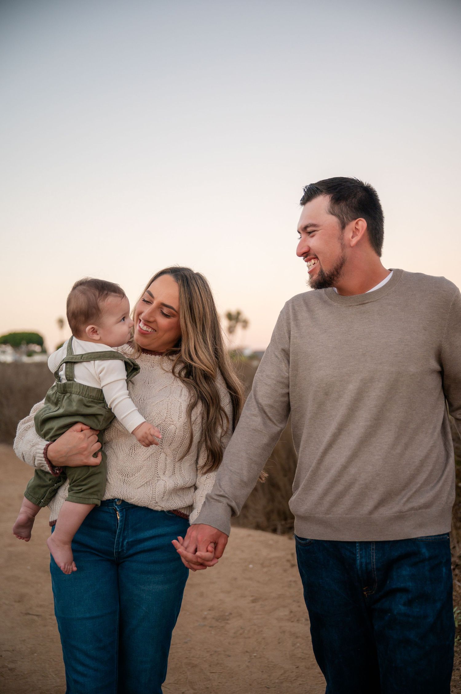 A family shares tender moments together at sunset in a desert landscape, wearing casual sweaters and jeans.