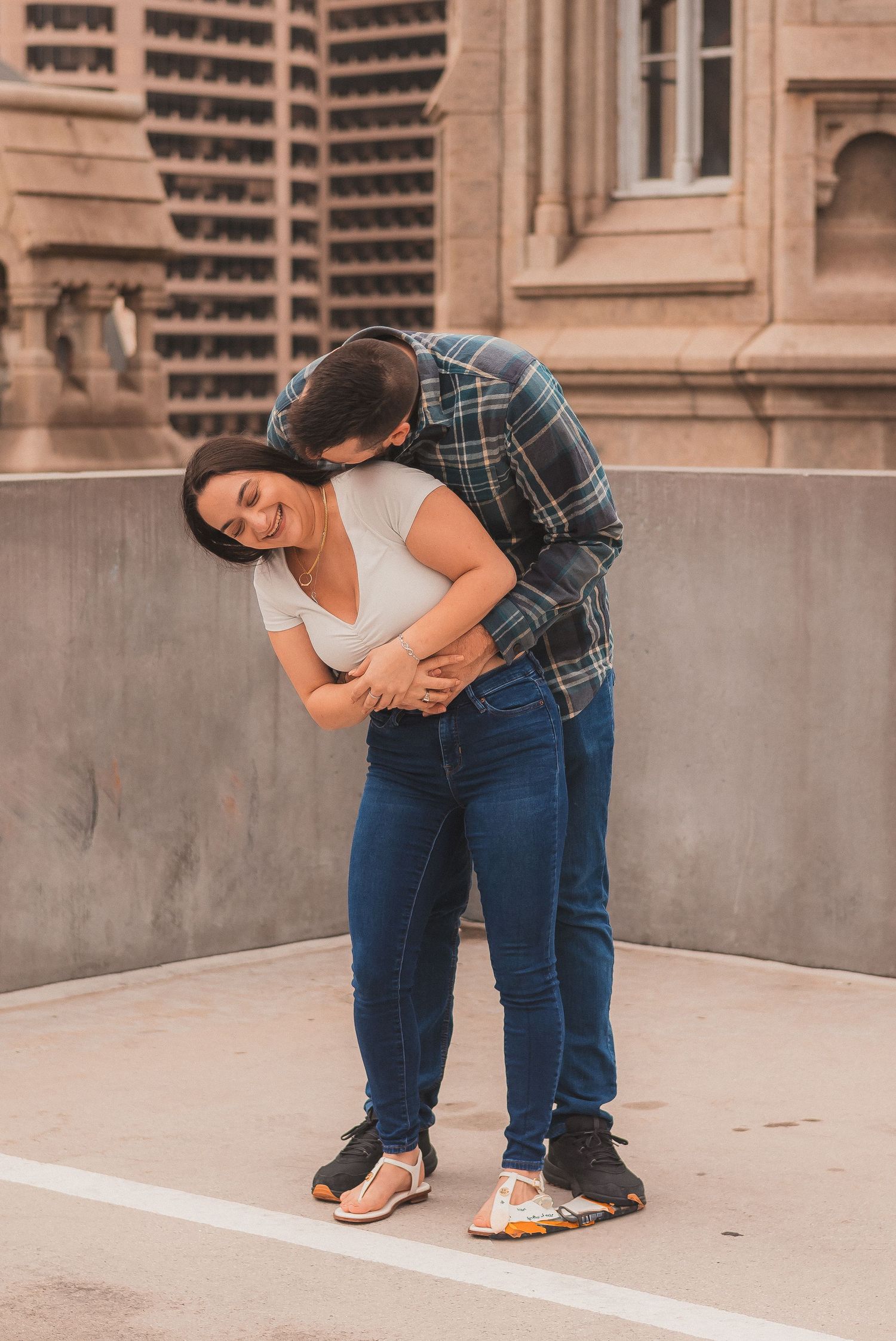 A couple shares a tender moment while leaning against a concrete wall near gothic architecture.