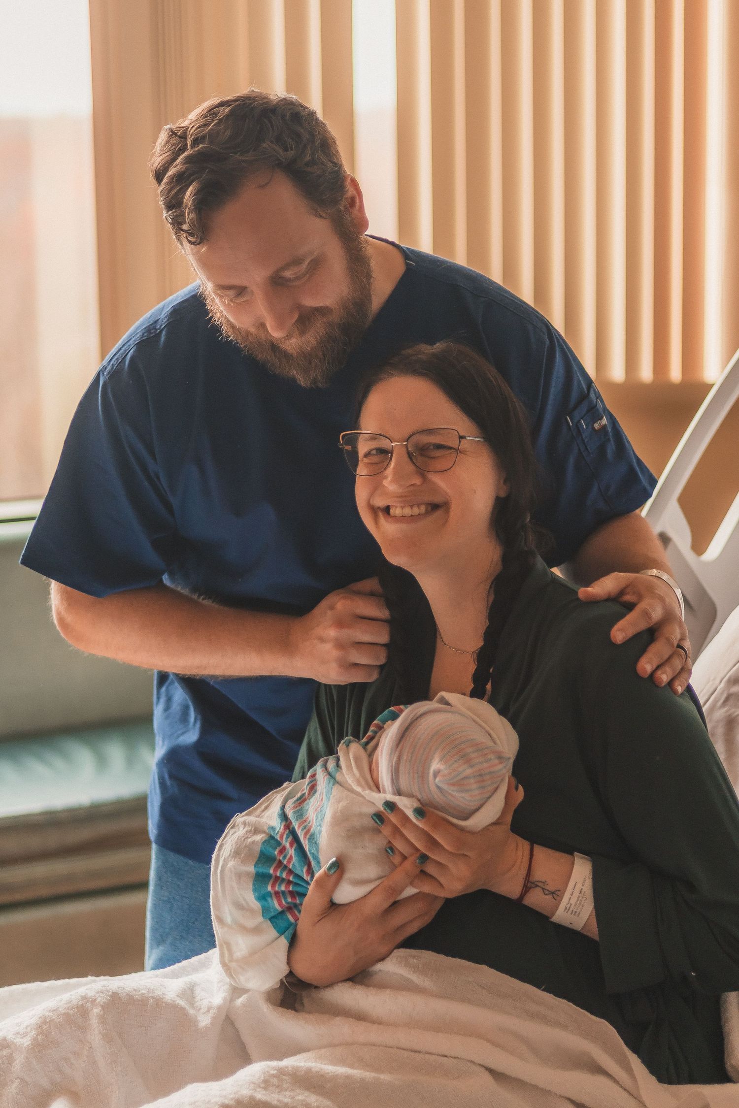 New parents bond with newborn baby in hospital room setting.
