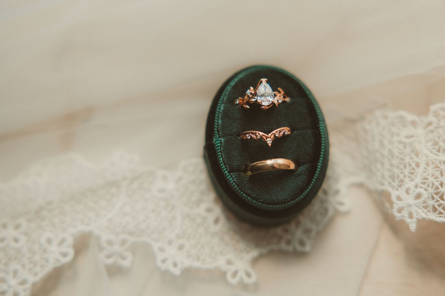 Three vintage engagement rings rest in a dark green velvet ring box on delicate lace fabric.