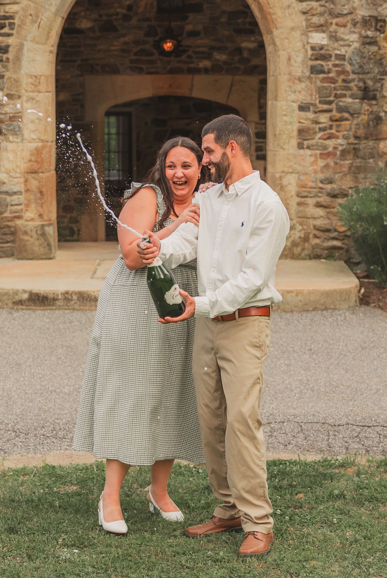 A couple celebrates with champagne spraying outside a stone archway at a rustic venue.