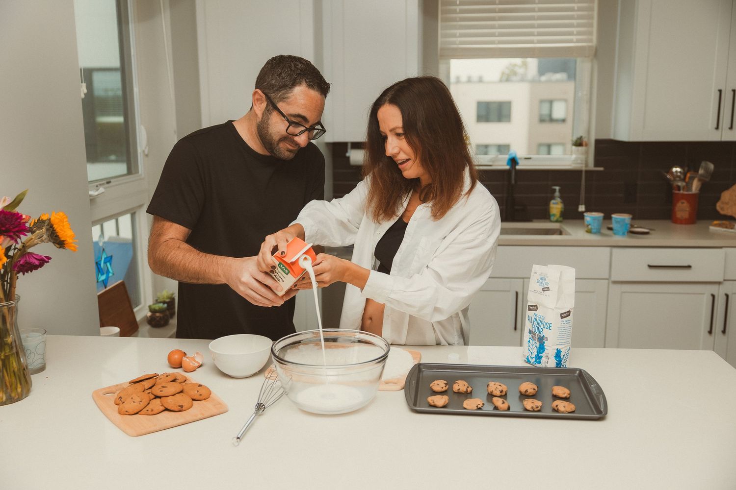 Two people in a modern kitchen work together preparing ingredients at a marble countertop with kitchen appliances.