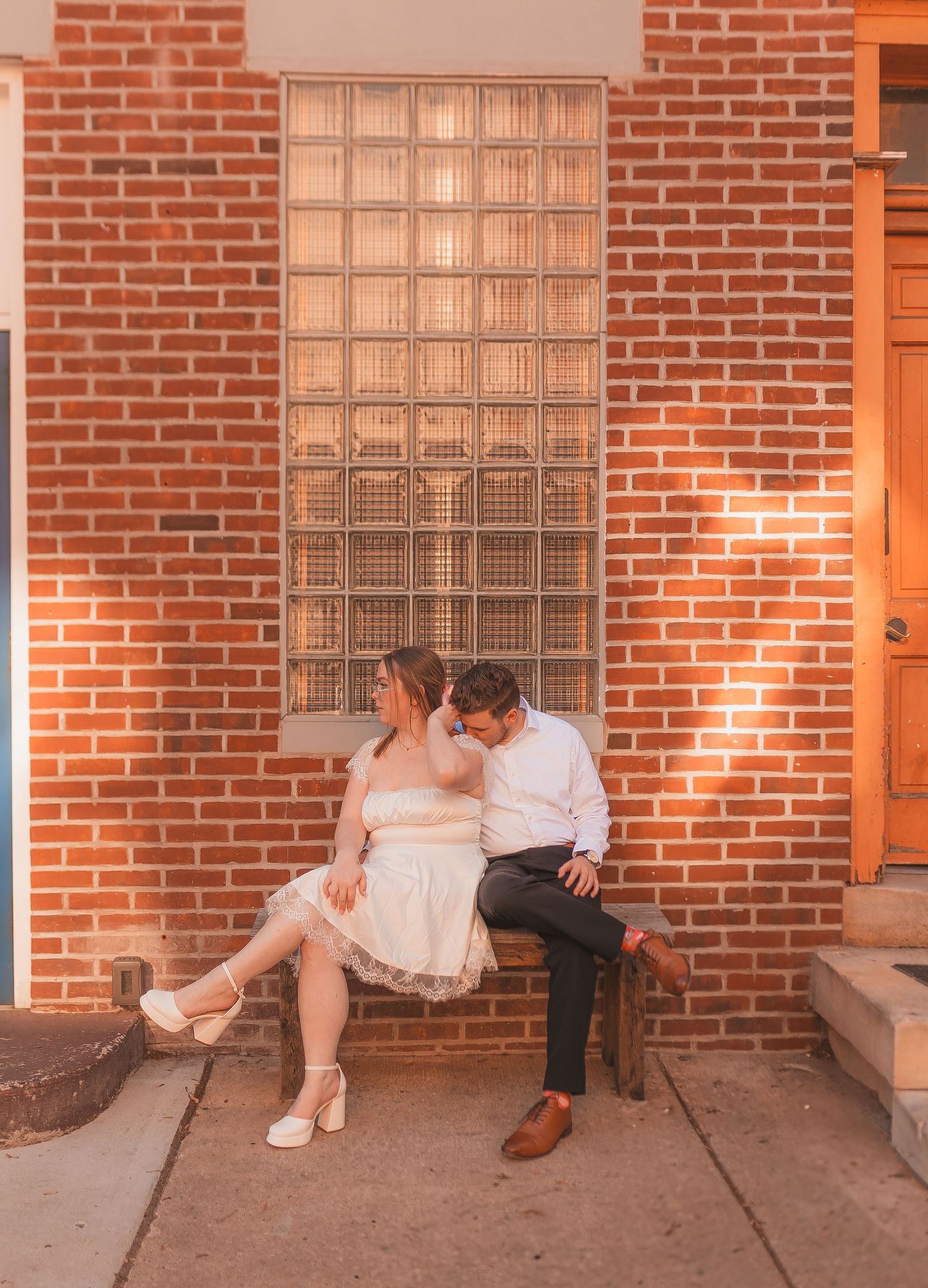 A couple sits together on a brick ledge during a romantic sunset photoshoot.
