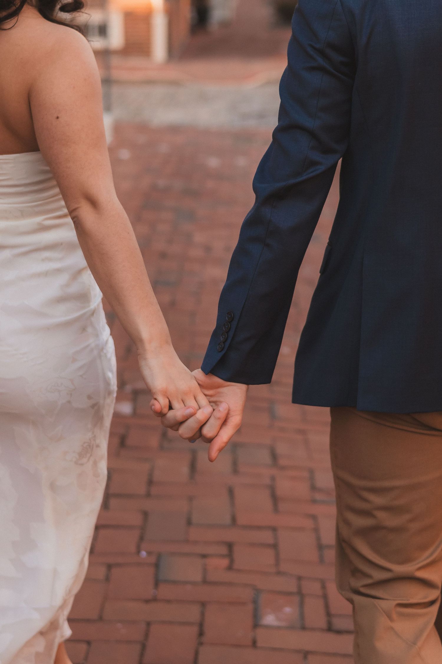 Close-up of a couple holding hands while standing on brick pavement.