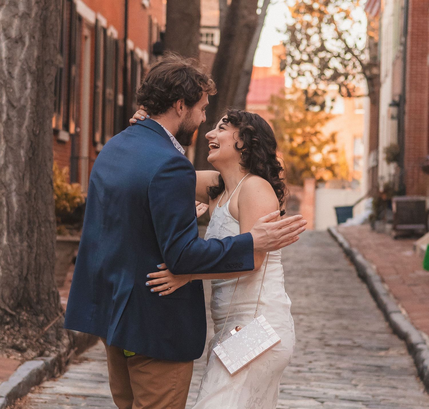 A couple embraces and laughs together on a historic cobblestone street.