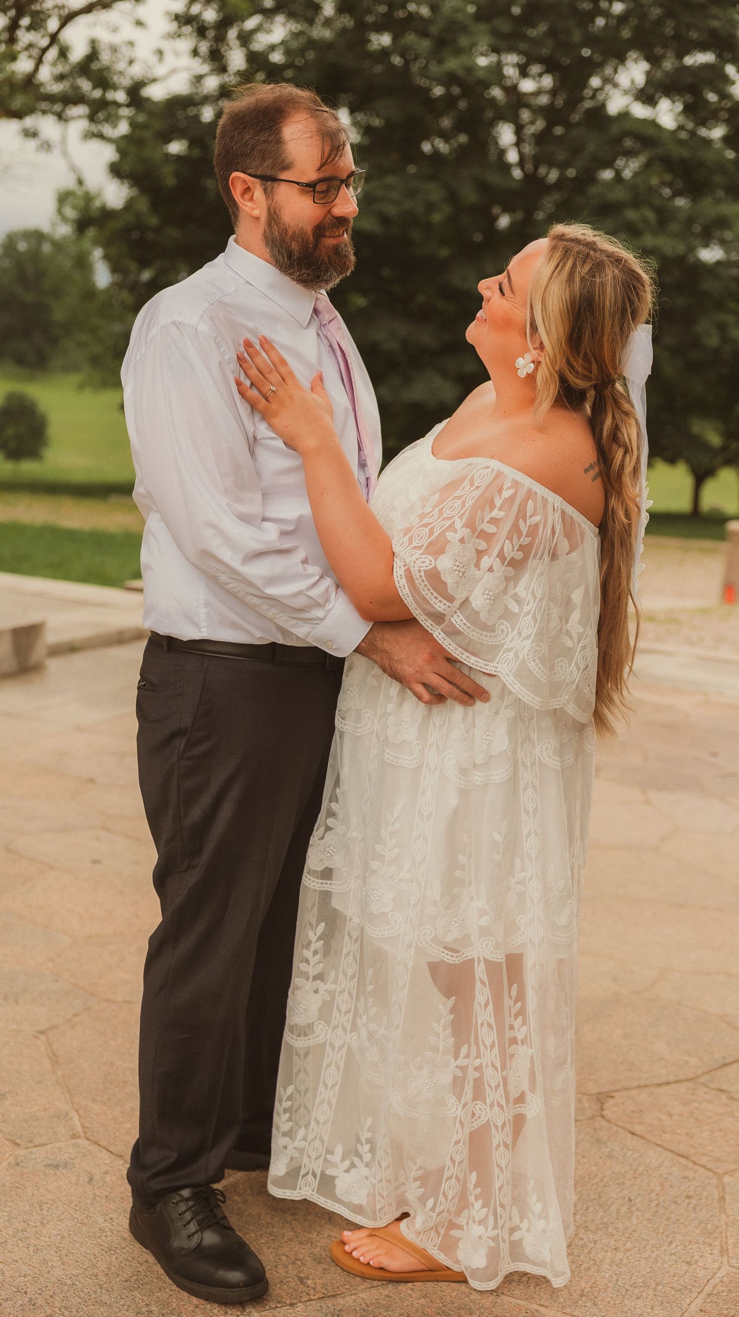 A newlywed couple shares a romantic moment outdoors, with the bride wearing a beautiful lace gown and the groom in white shirt.