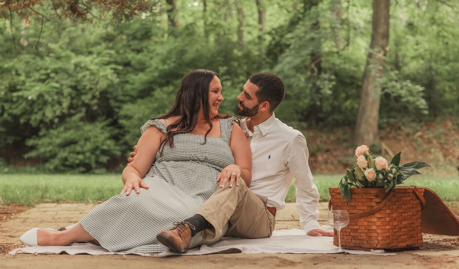 Couple enjoying a romantic picnic on a blanket in a lush green park with wicker basket and flowers.