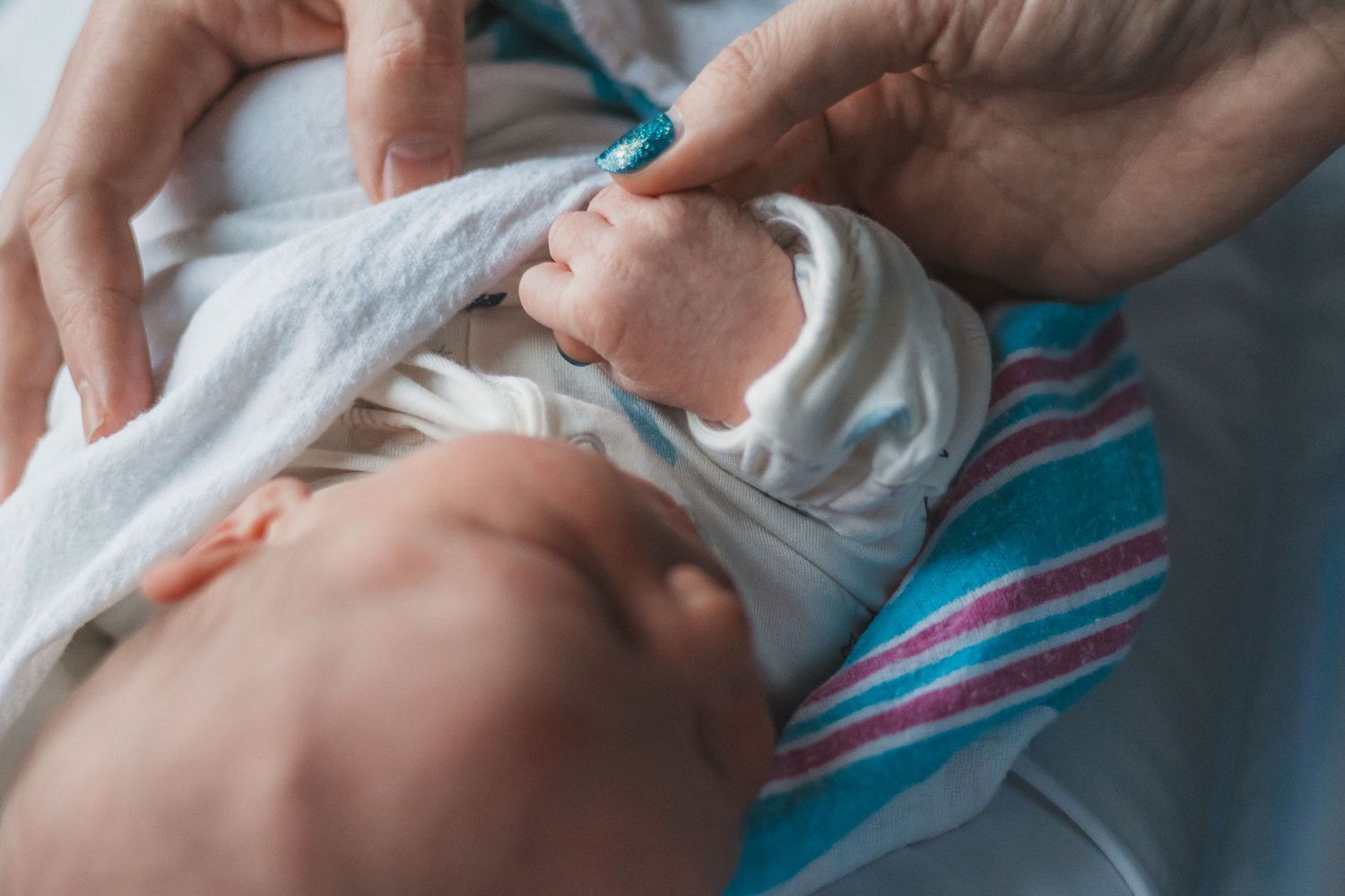 Gentle hands caring for newborn baby wrapped in striped blanket.