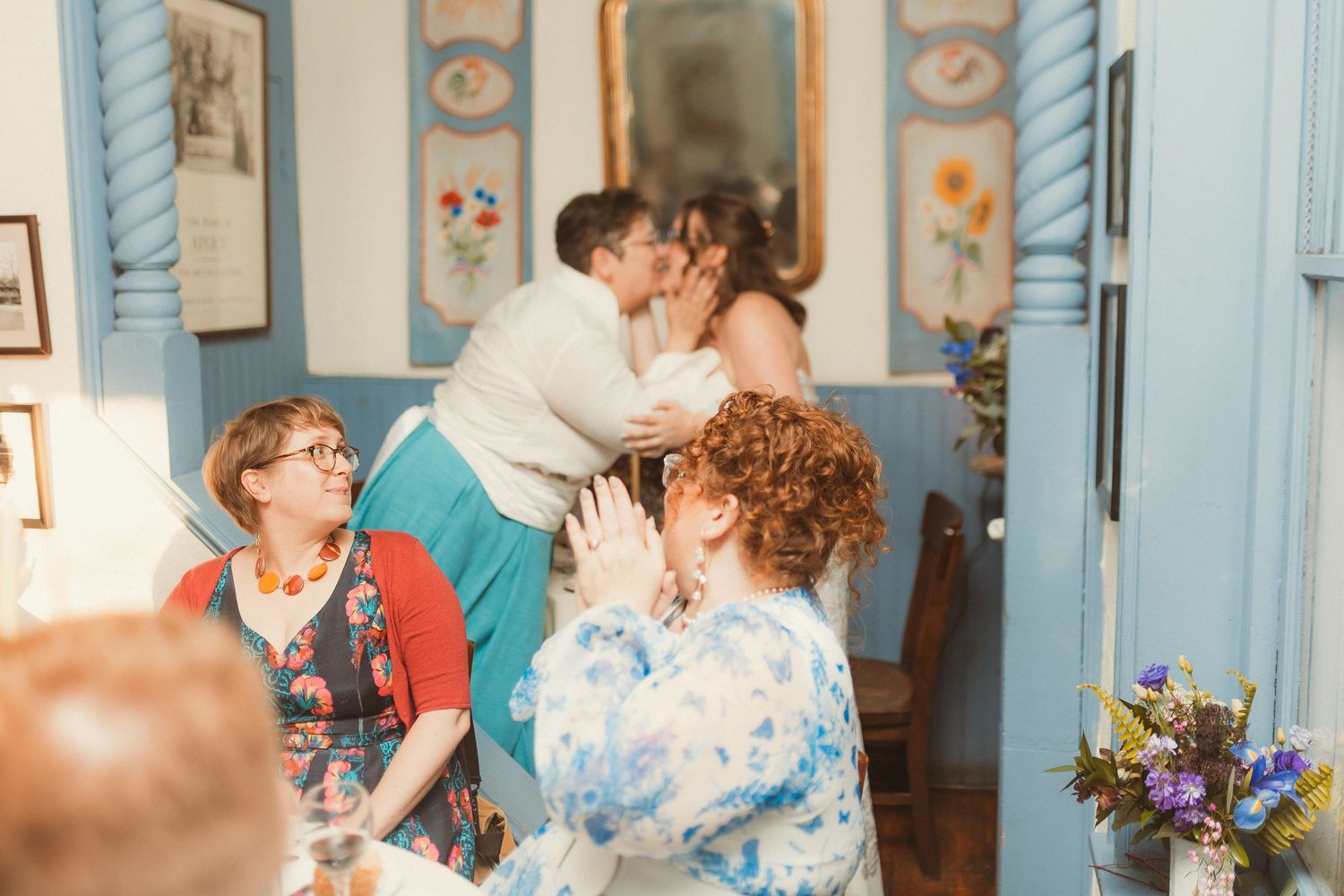 Wedding guests laugh and celebrate in a blue-decorated room with floral arrangements.