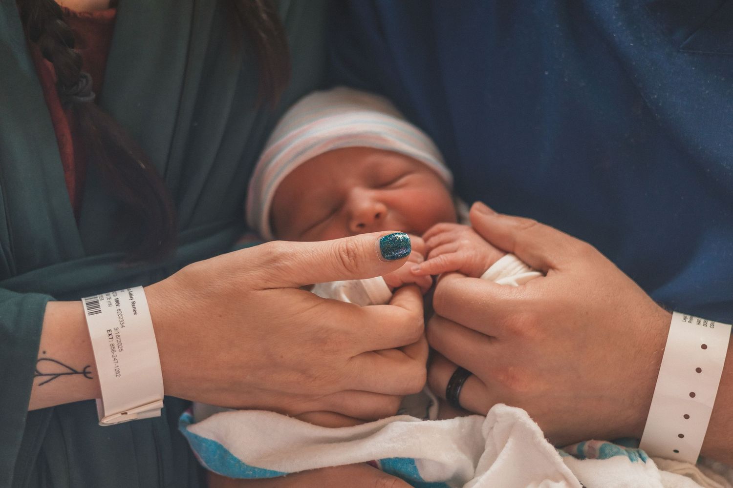 Close-up of hands holding newborn baby in hospital setting.