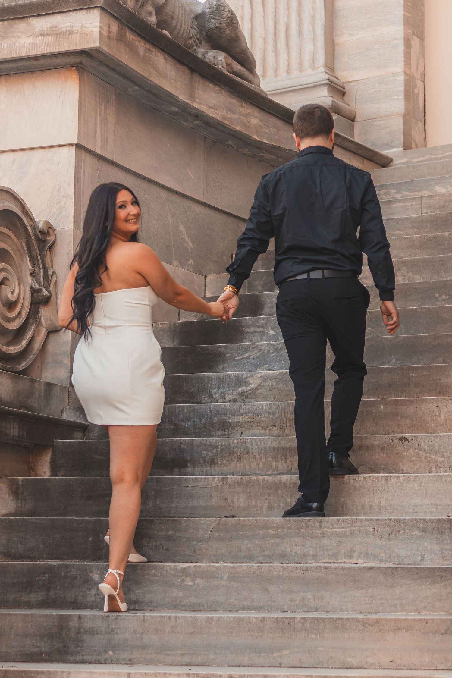 A couple climbing stone steps together in formal attire holding hands.