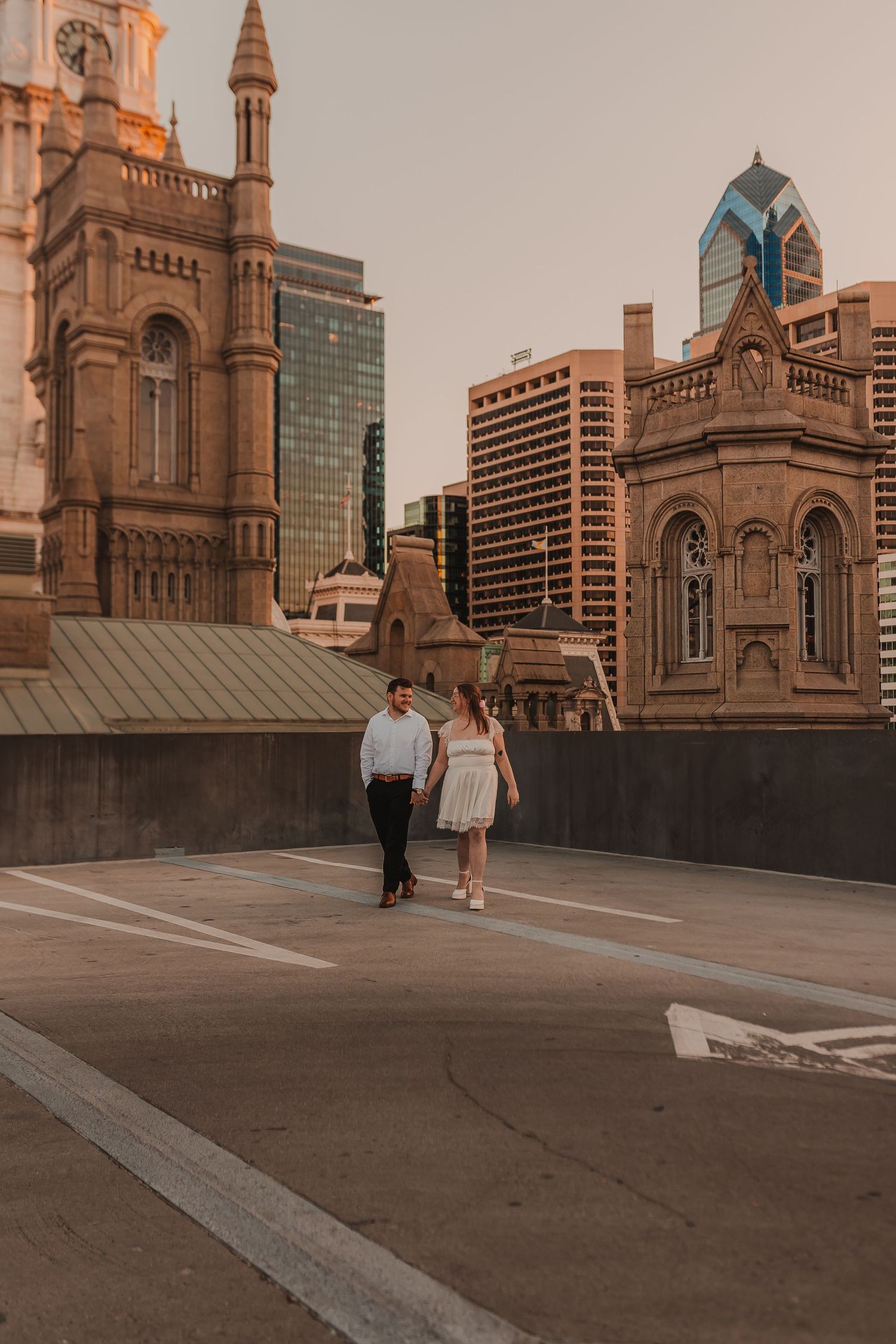 Couple walking on urban rooftop with historic church architecture and modern buildings in background.