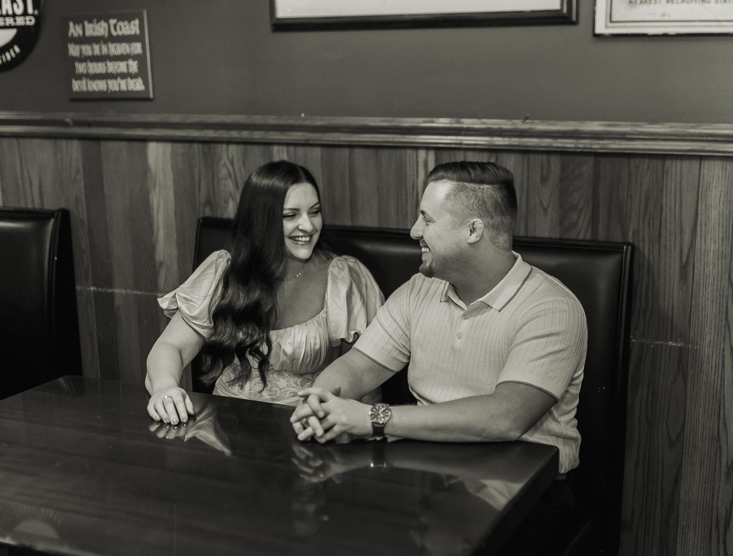 A couple shares a candid black and white moment together at a restaurant booth, smiling and engaged in conversation.