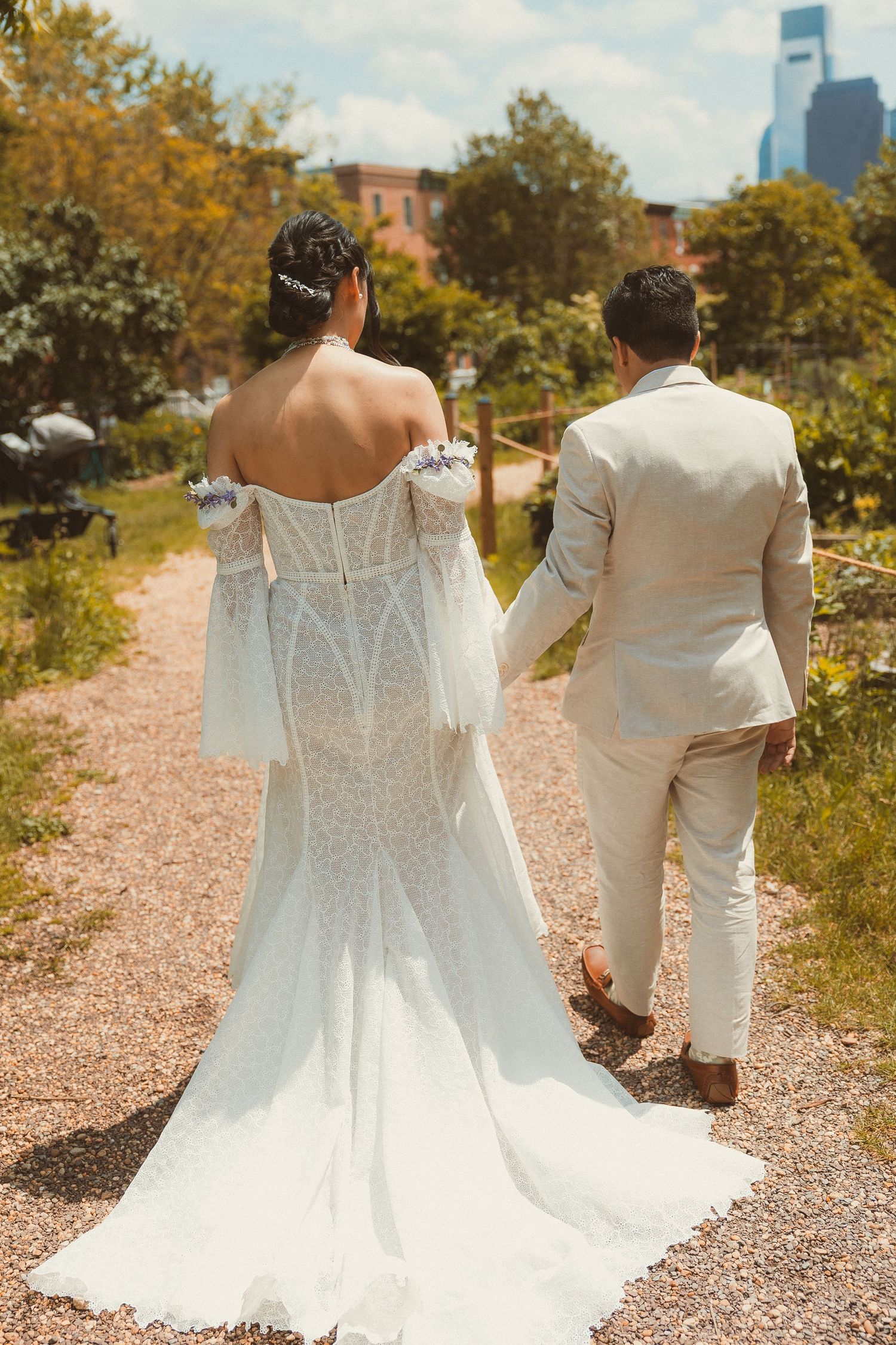 Romantic wedding couple walking down garden path wearing white dress and light colored suit on sunny day.
