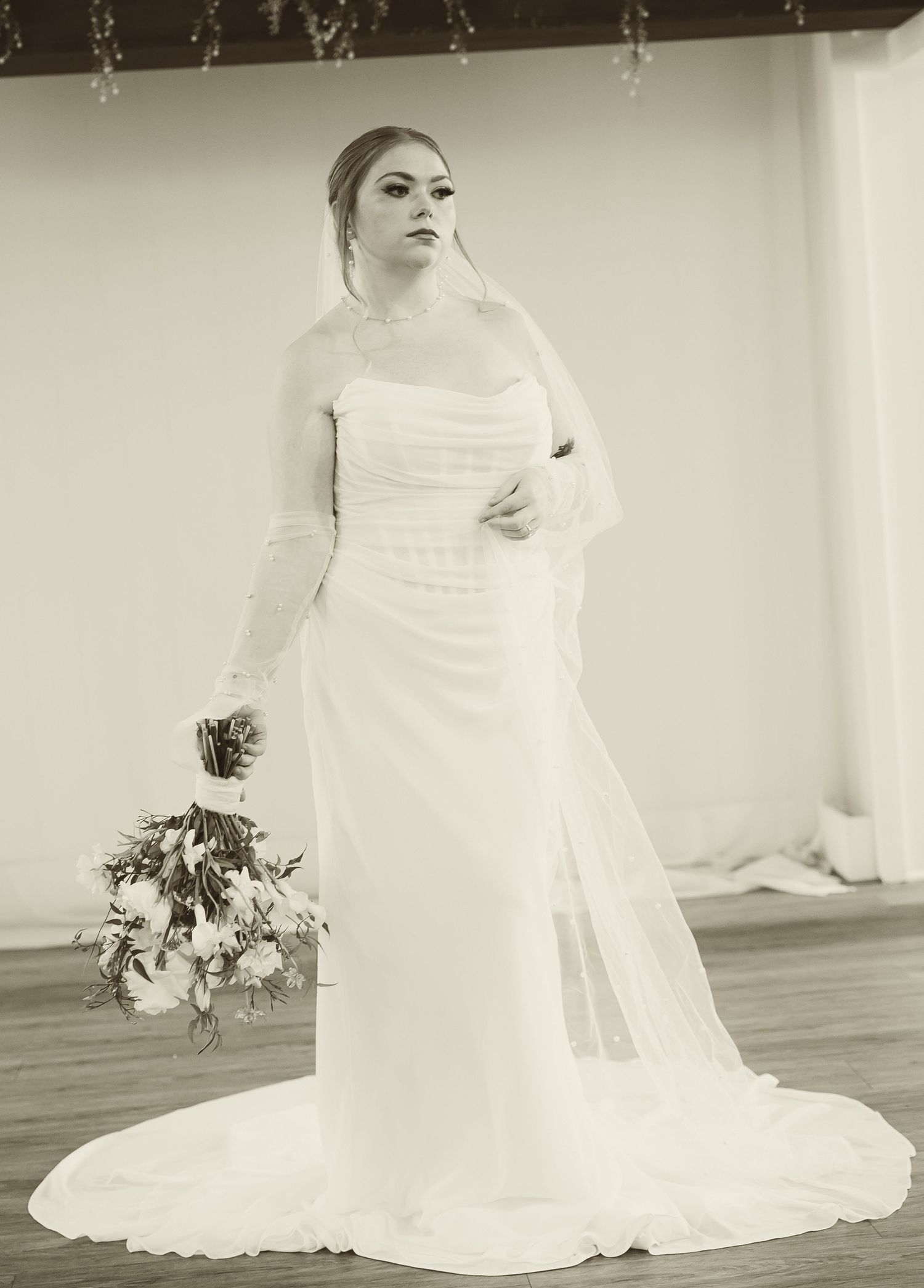 A classic black and white bridal portrait showcasing a strapless wedding gown with a flowing train and floral bouquet.