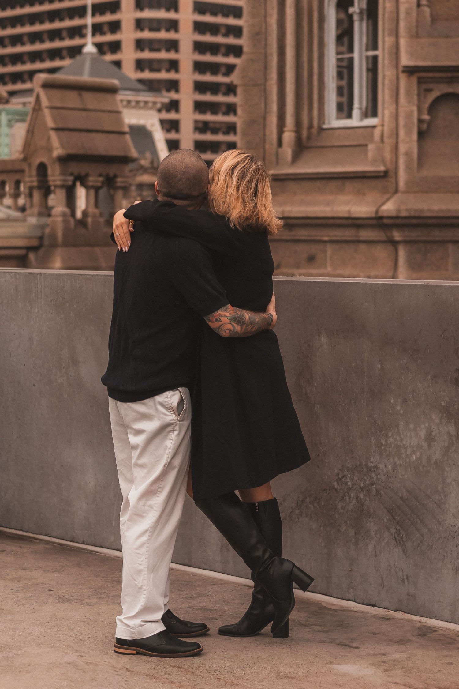 Couple embracing near historic architecture with modern skyscrapers in background.