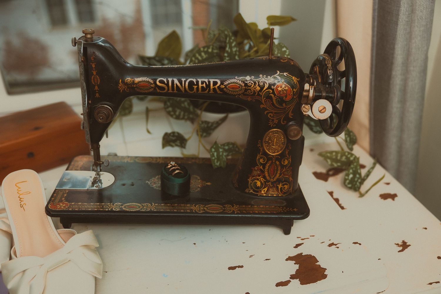 Vintage black Singer sewing machine with ornate gold decorations sits on white surface with fabric nearby.