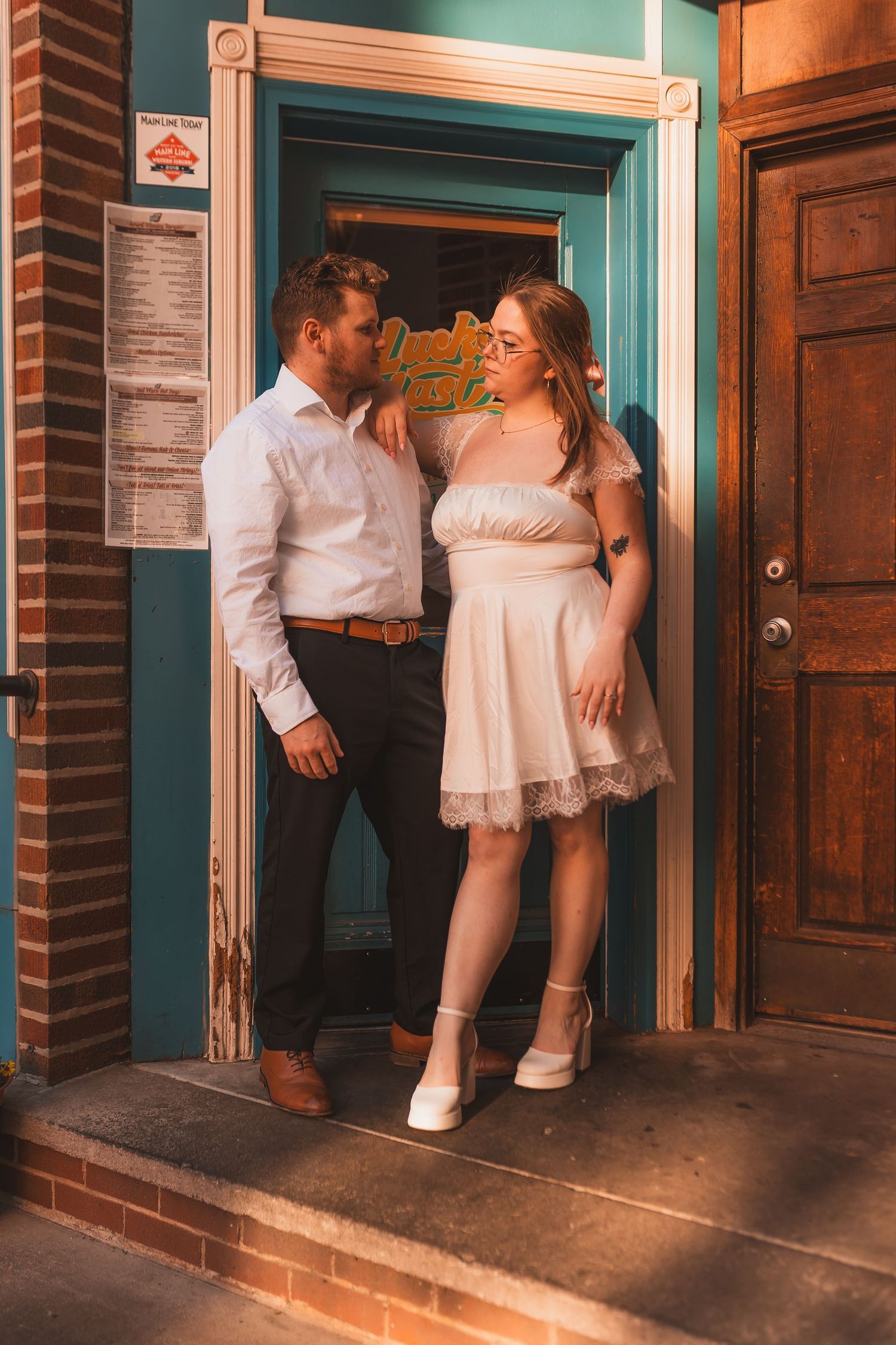 A couple in formal wear poses in a turquoise doorframe of a brick building.