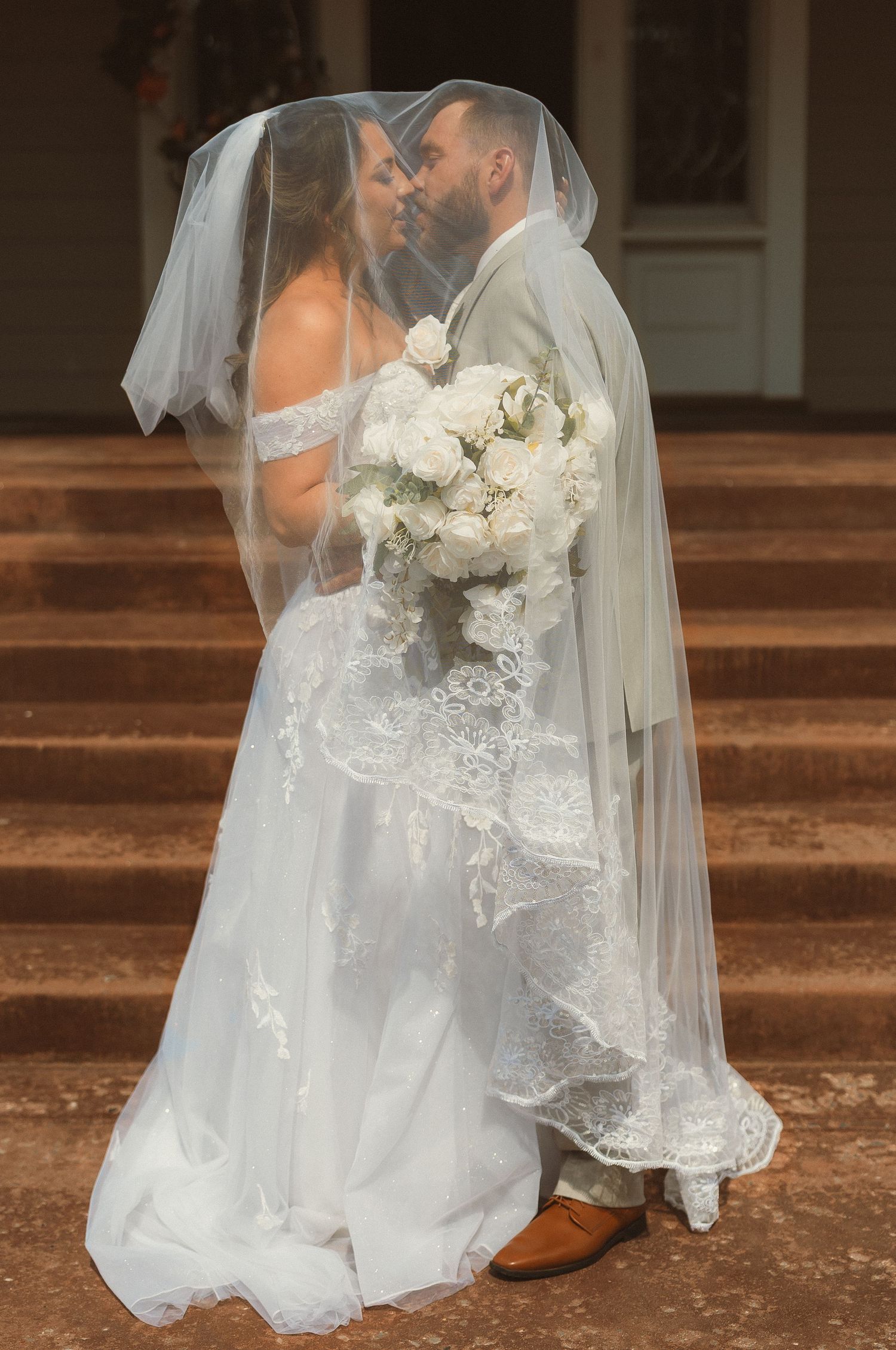 A tender moment between newlyweds under a flowing veil on stone steps.