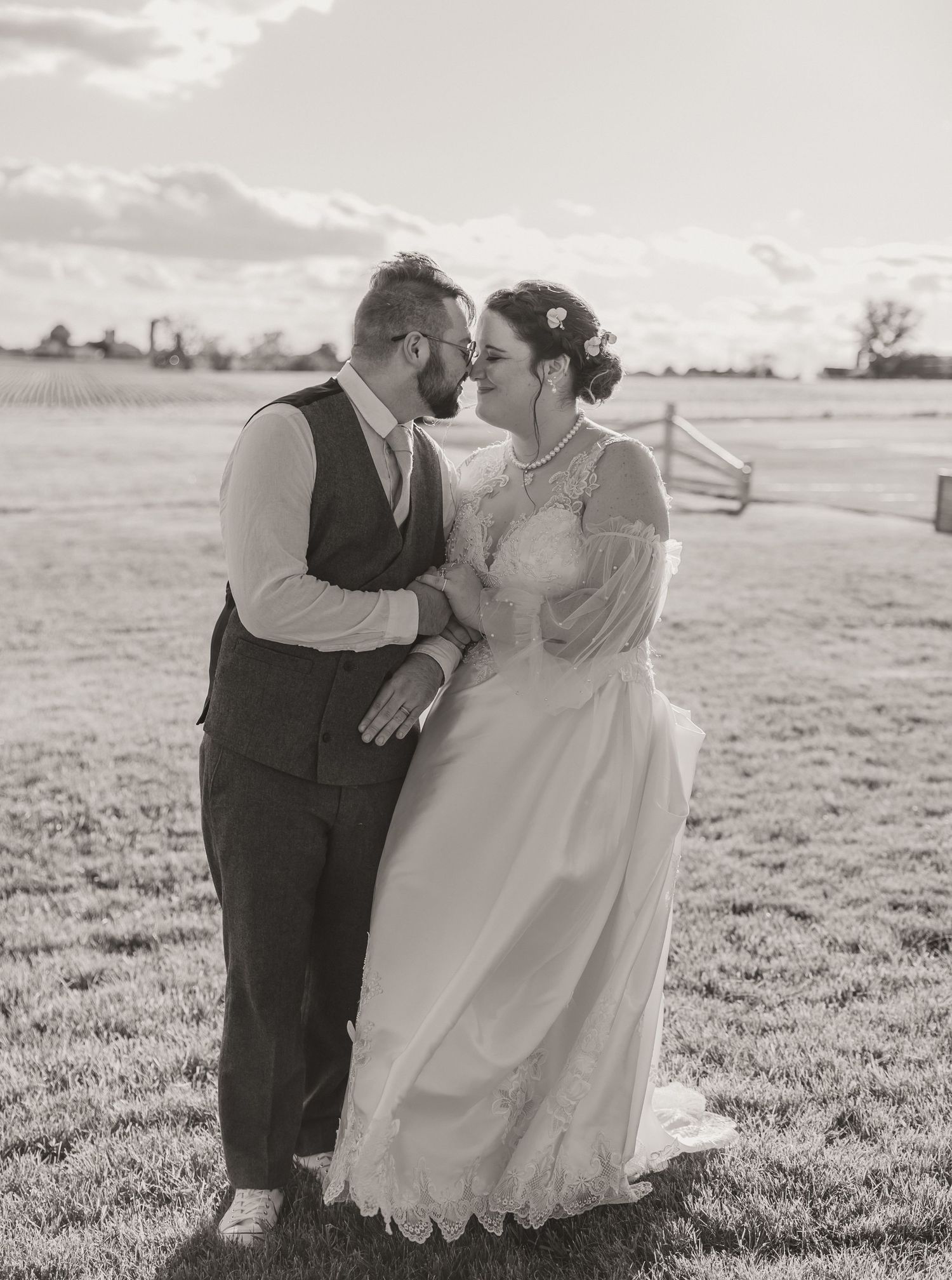 A romantic black and white wedding photo of a couple embracing in a field on an overcast day.