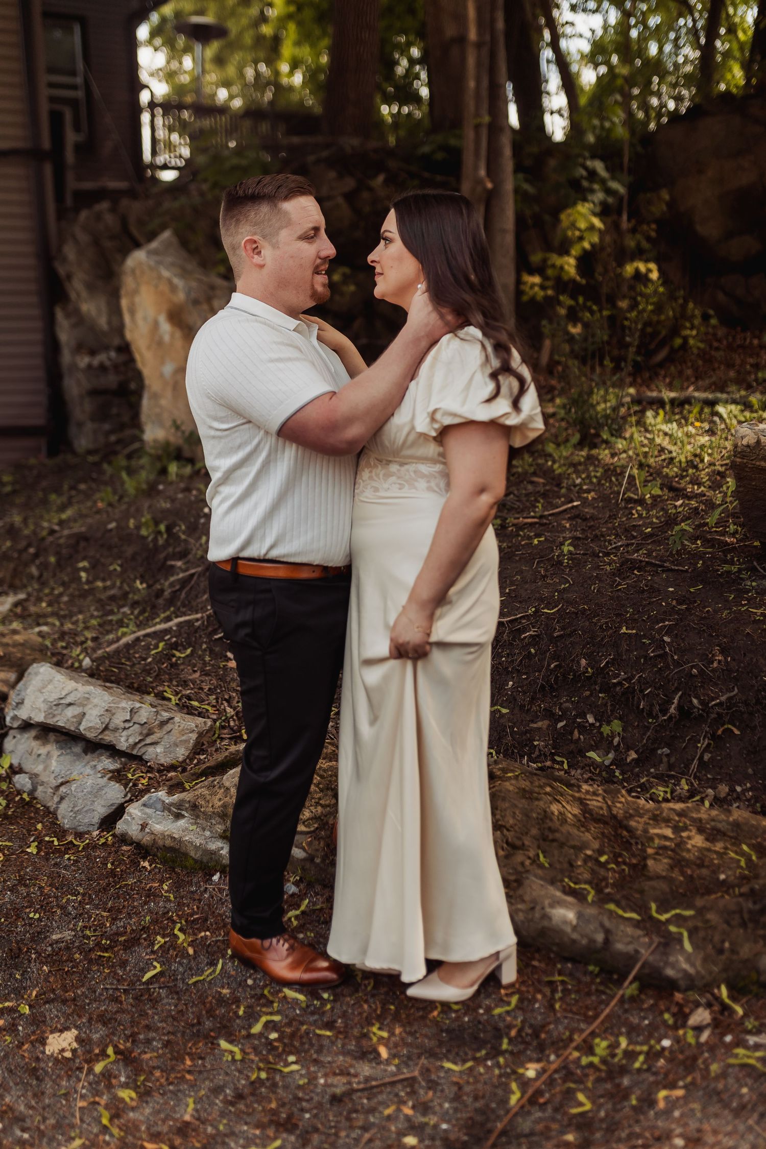 A romantic couple in cream colored outfits sharing an intimate moment together in a wooded outdoor setting.
