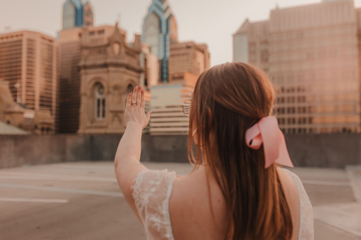 A person in a white dress looks out at the city skyline during golden hour.