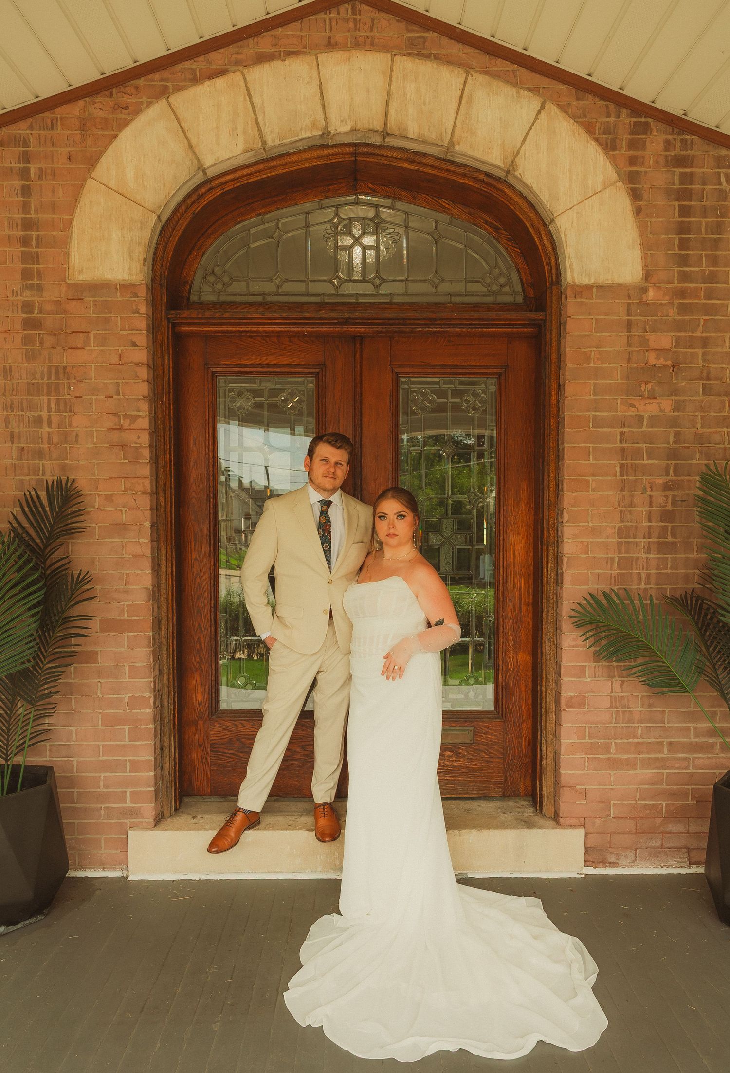 An elegant wedding photo series taken at a brick entrance with arched doorways and palm plants.