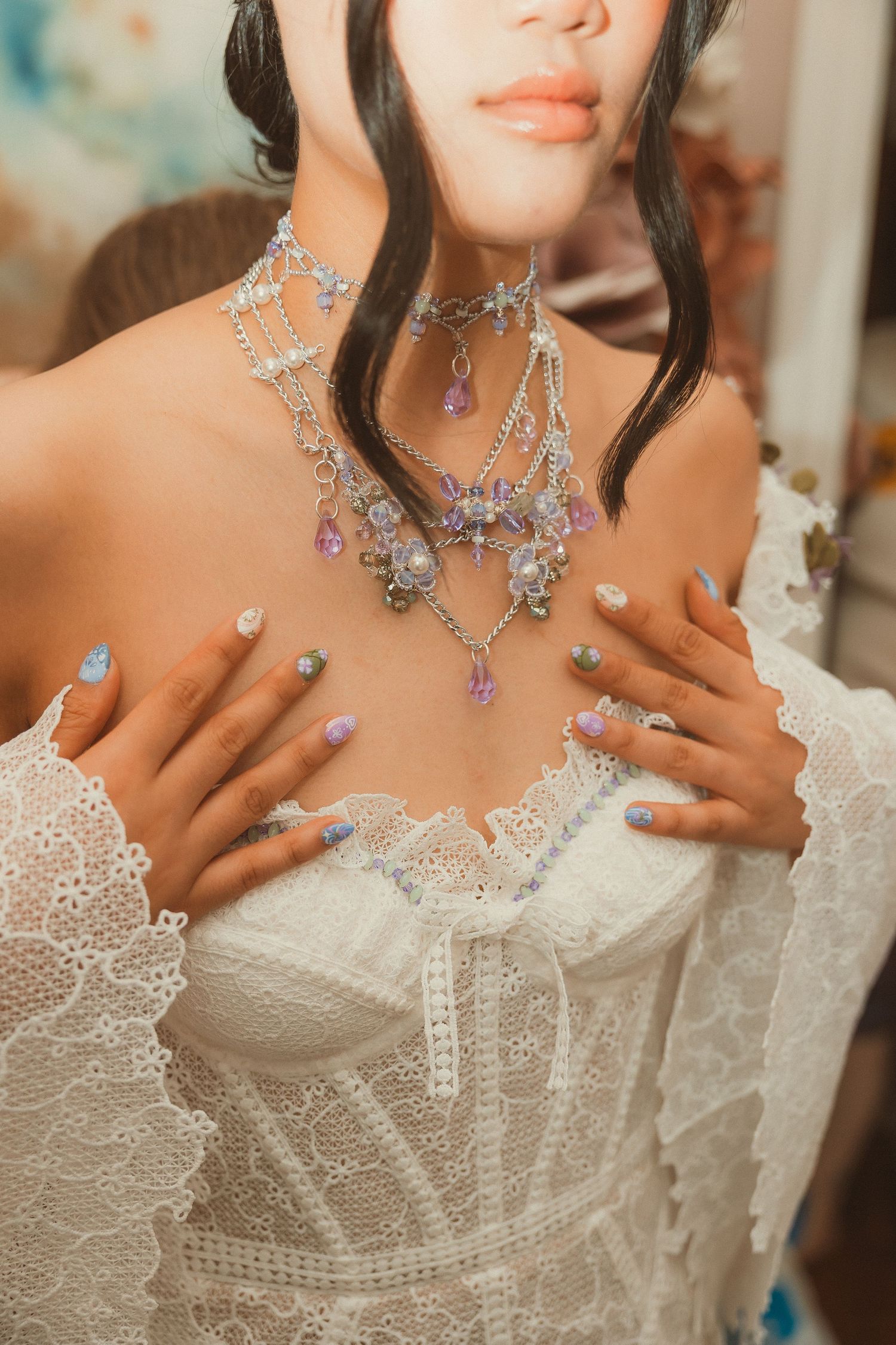 Elegant bridal details showing delicate lace corset, sparkly crystal necklace, and manicured nails in blue and purple polish.