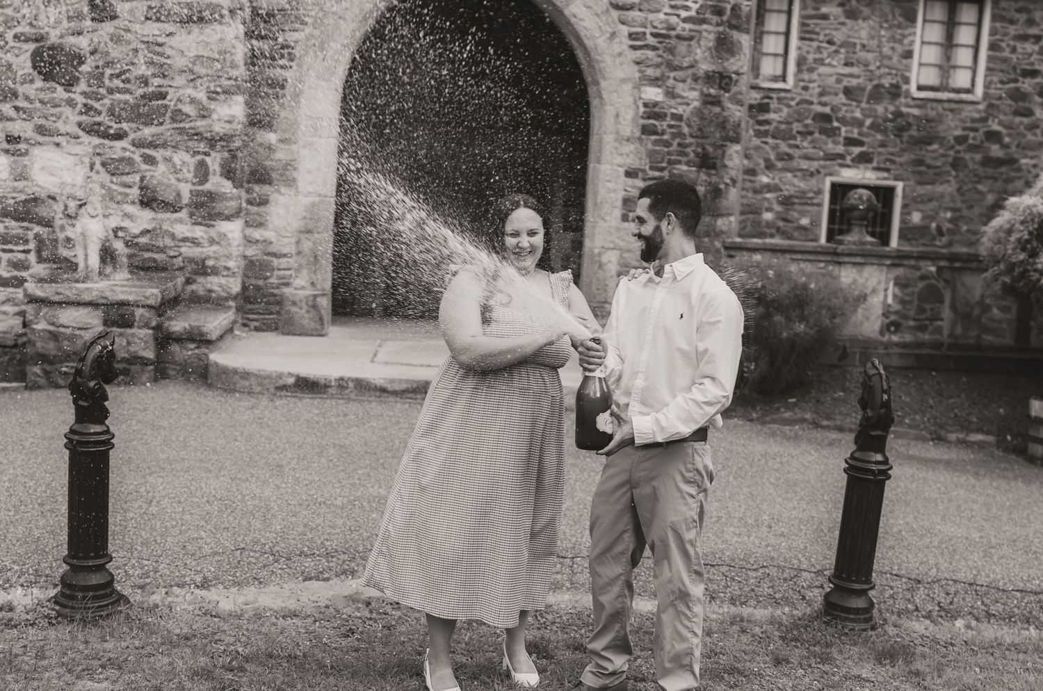 A couple shares a joyful moment together in front of a stone archway at a historic building.