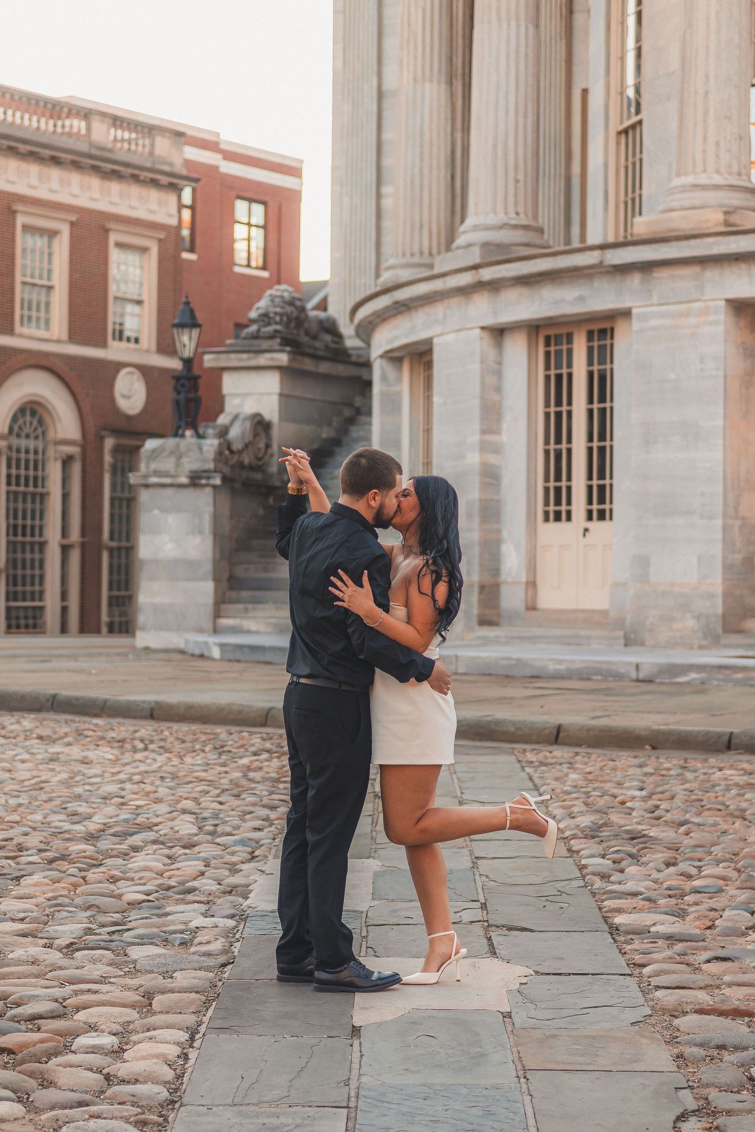 A romantic dance pose on cobblestone ground in front of a classical building.