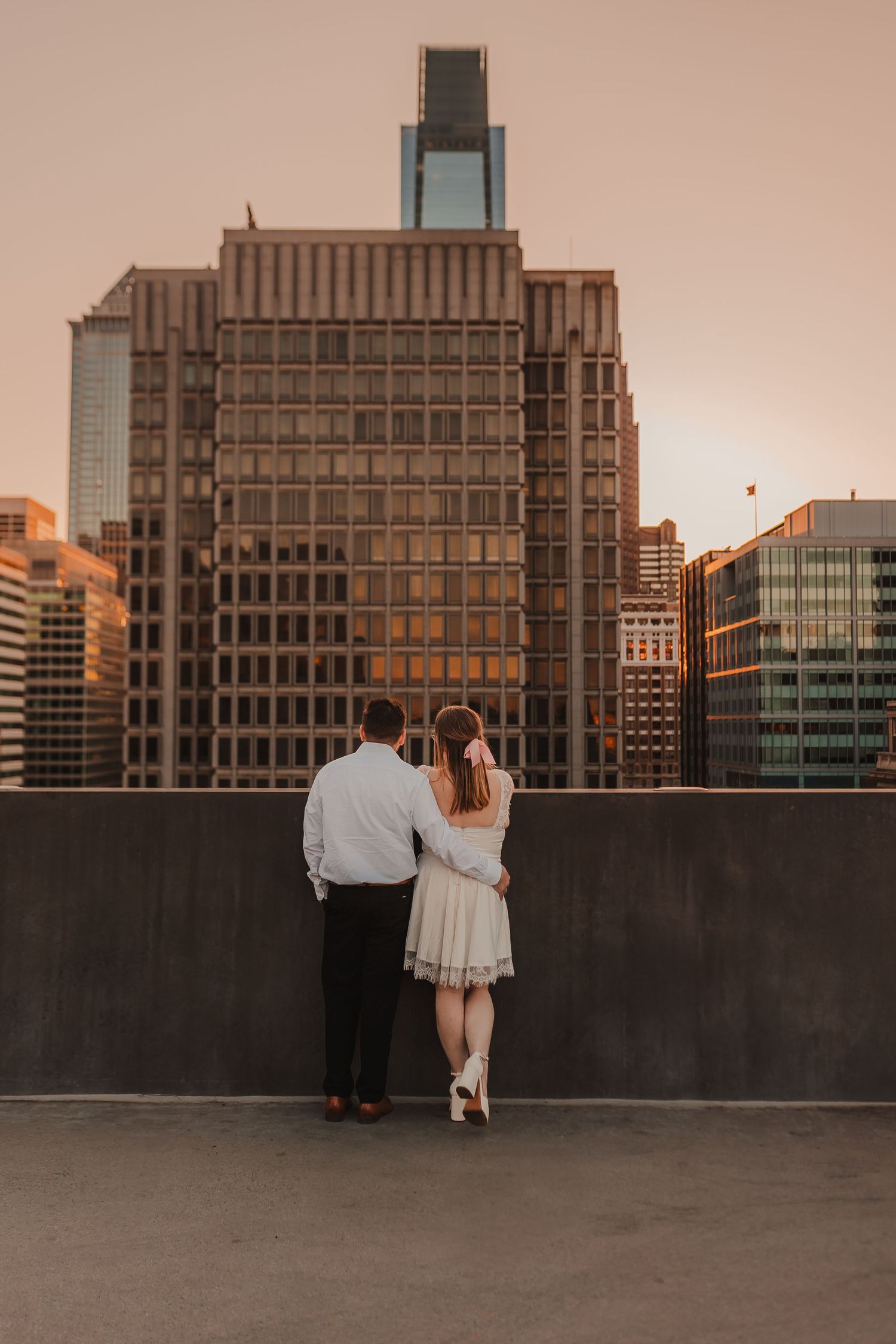 Couple overlooking city skyline from rooftop during golden hour.