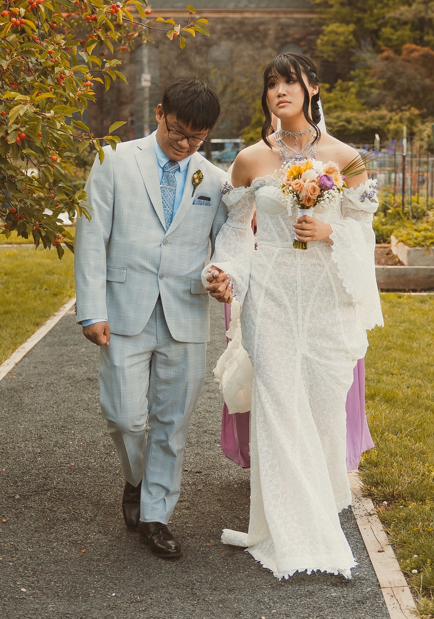 Two people walking together in wedding attire, with the bride holding a colorful bouquet on a garden path in autumn.