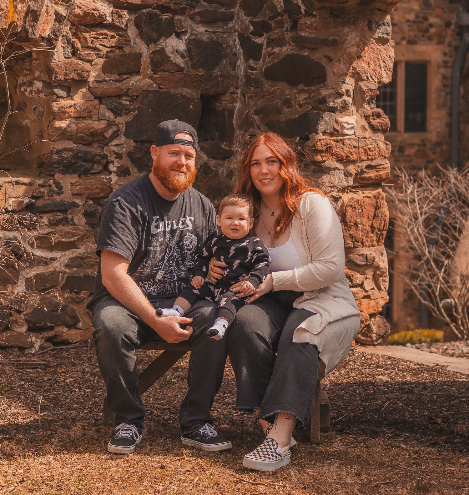 Family poses together against rustic stone wall background in autumn setting.