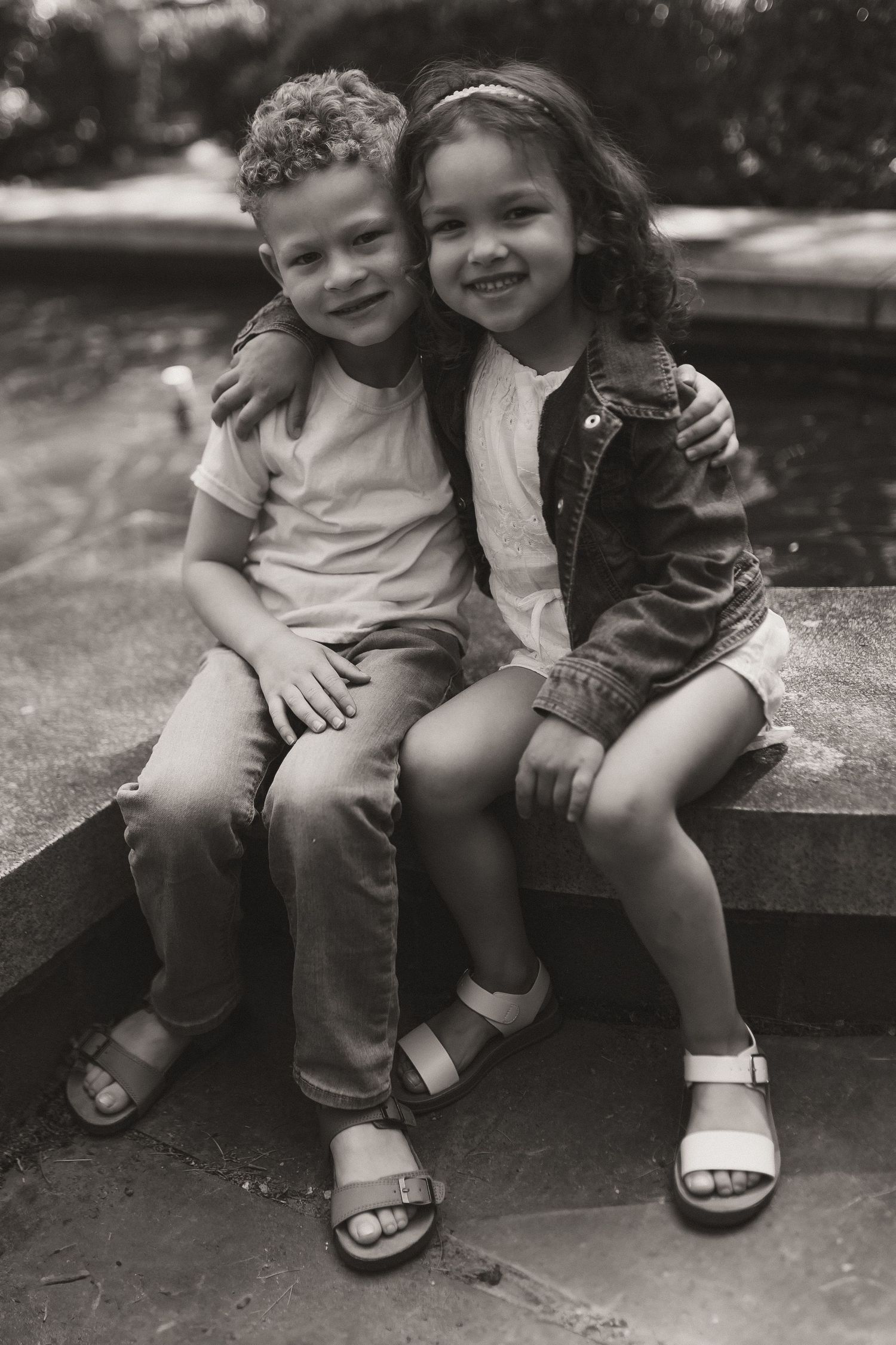 Black and white vintage photograph of two young children sitting together and smiling outdoors.