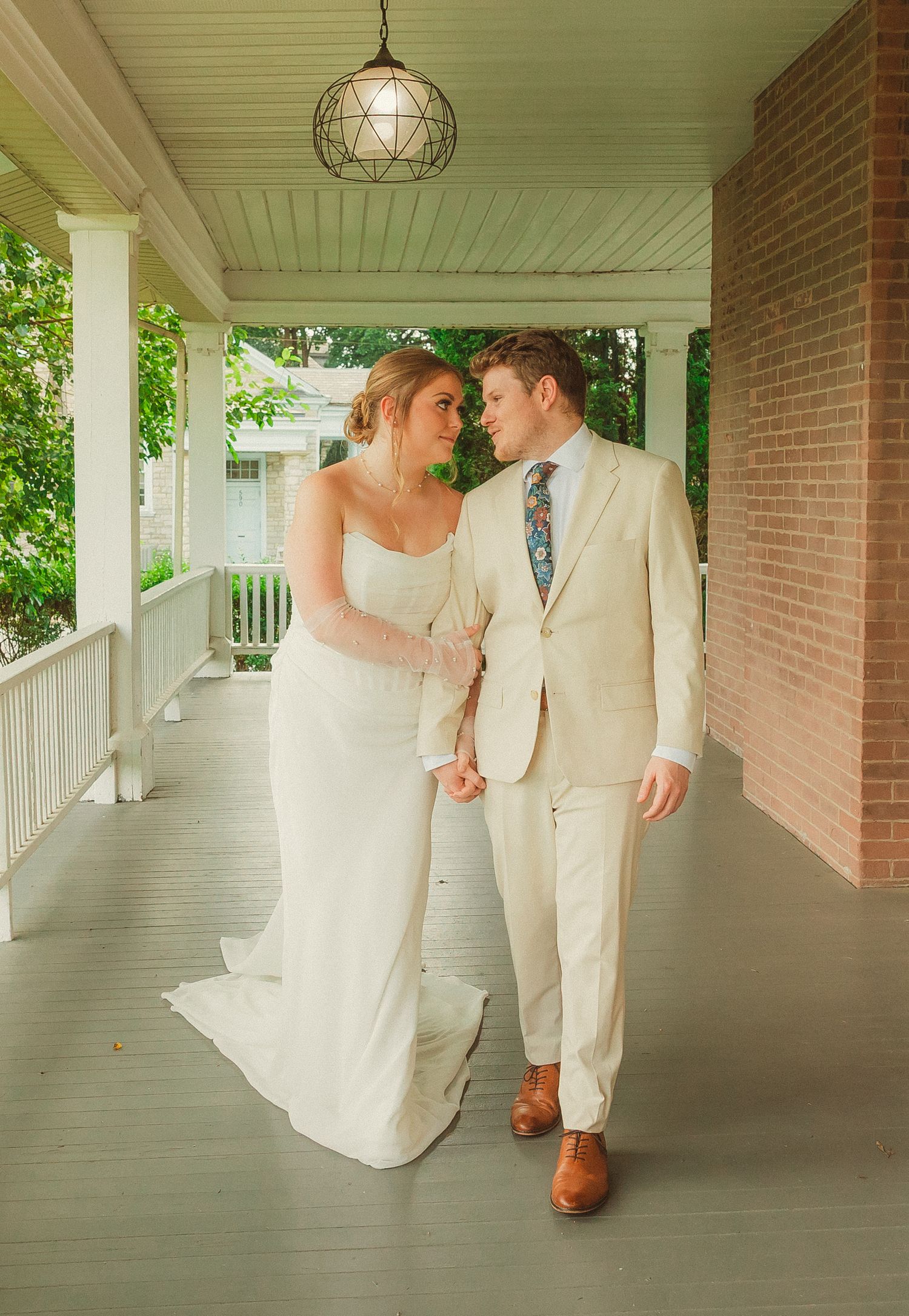 A romantic wedding sequence showing a couple in white walking and embracing along a covered brick porch with columns.