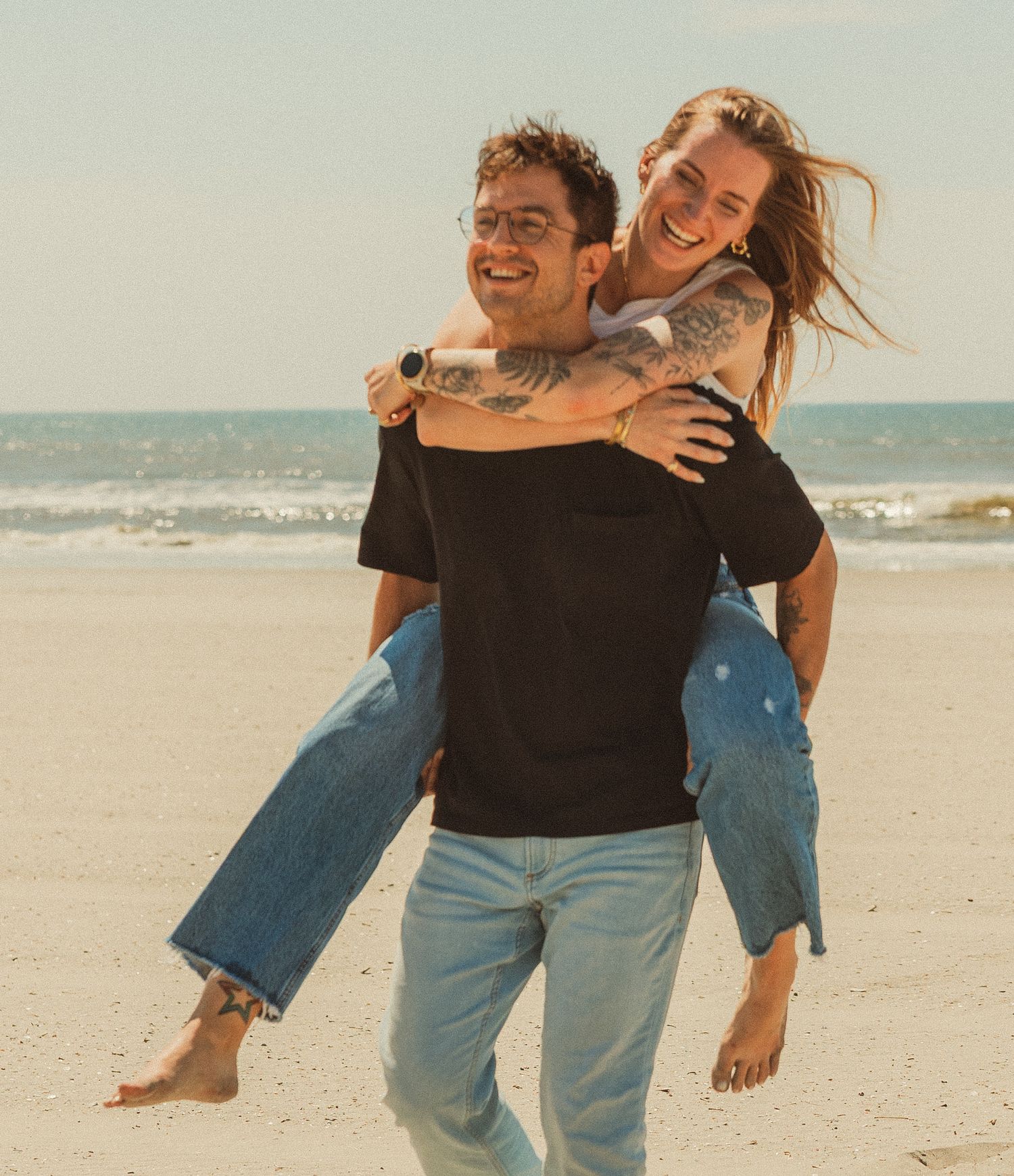A playful couple sharing joyful moments together while running and embracing on a sunny beach.