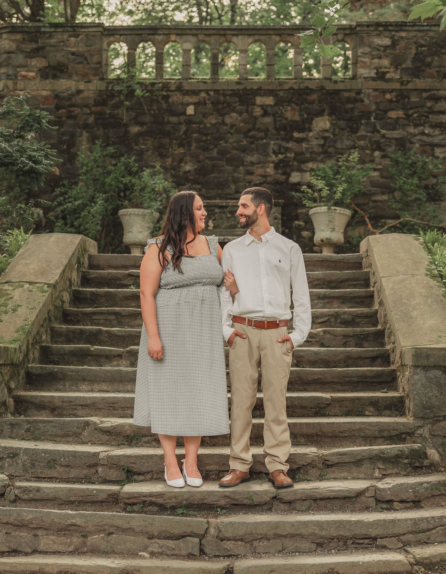 A couple sits and poses on stone steps in front of a rustic wall during a romantic outdoor photoshoot.