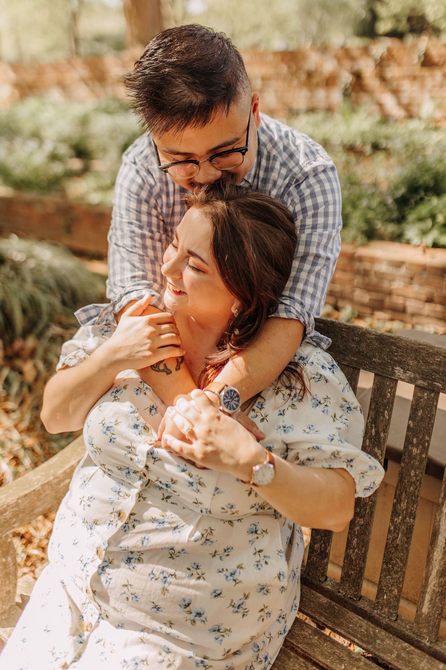 A romantic couple shares an intimate moment while sitting on a wooden bench in a garden setting.