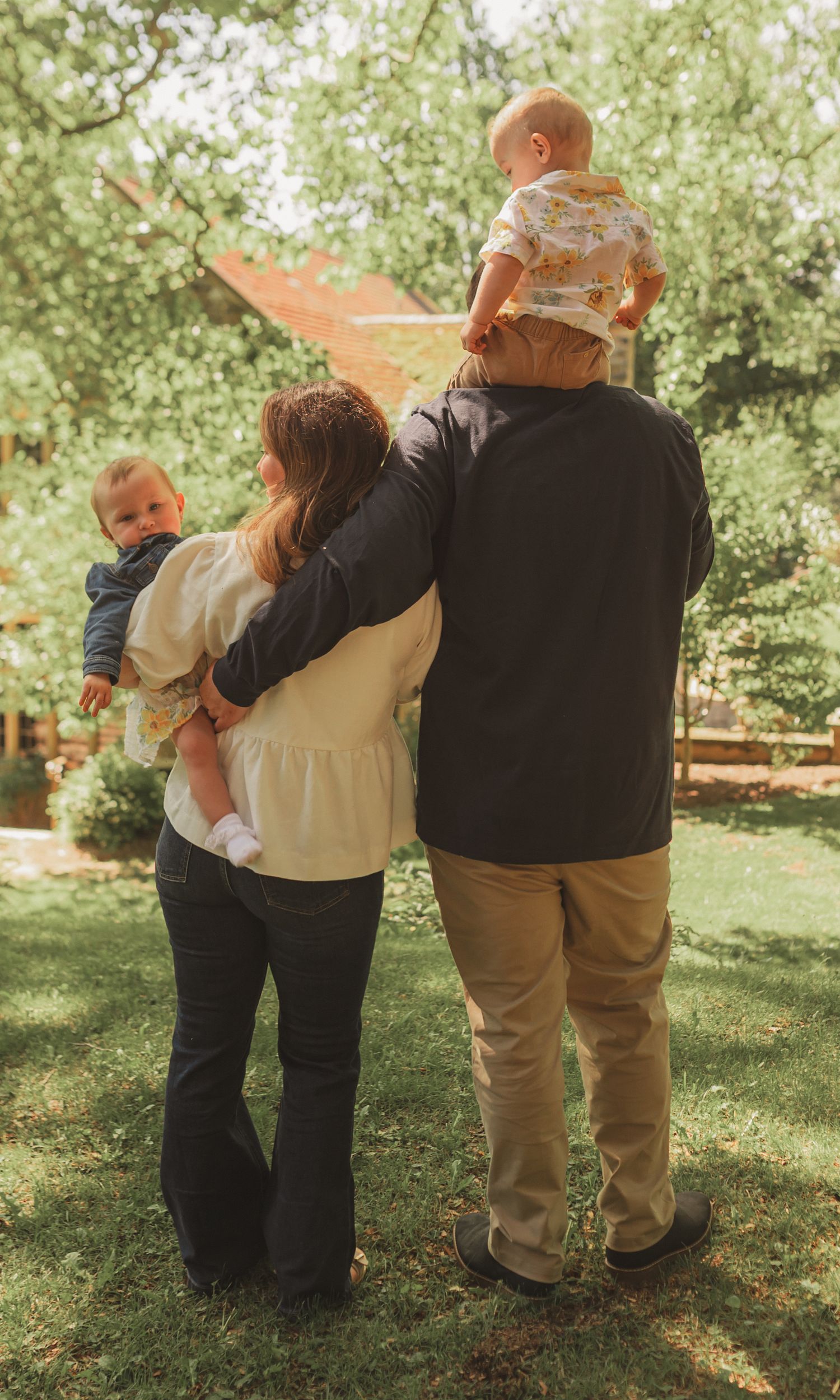 A family enjoying a sunny day together in a backyard garden setting with lush green trees in the background.