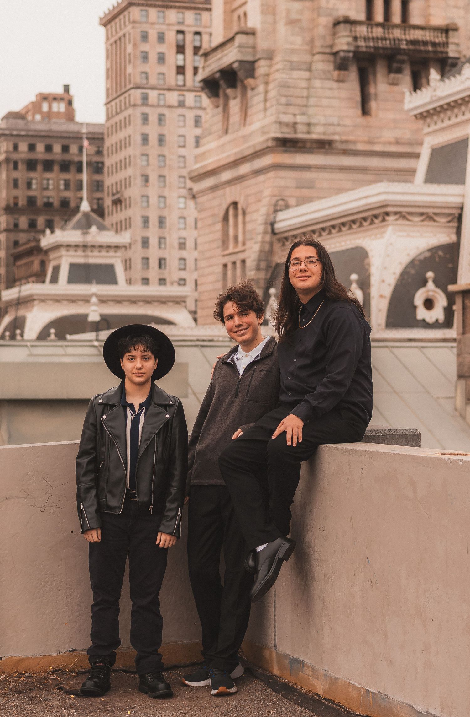 Three friends pose casually against a vintage urban backdrop with historic architecture.