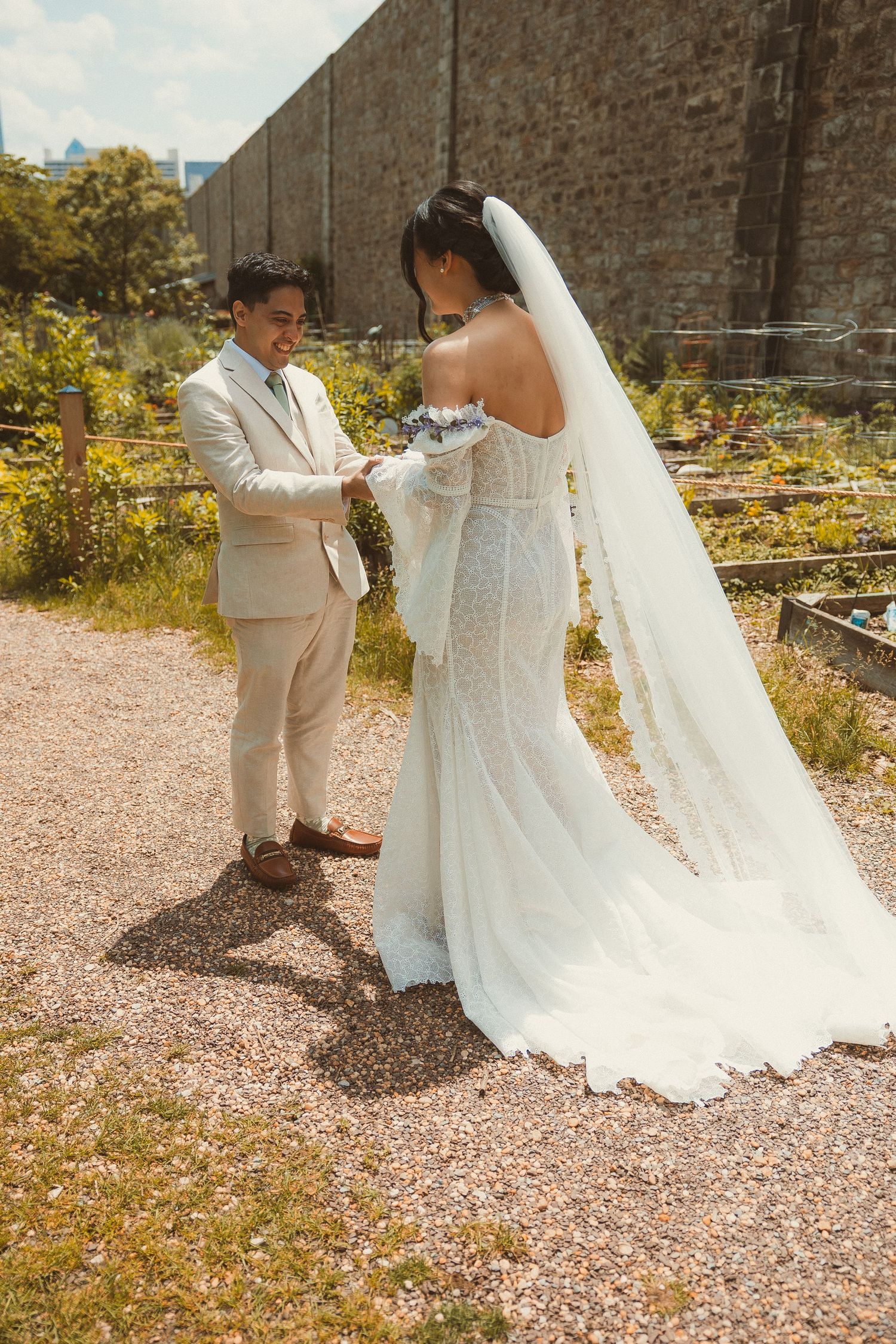 Elegant wedding ceremony in a garden setting with a long flowing white dress and veil against brick wall.